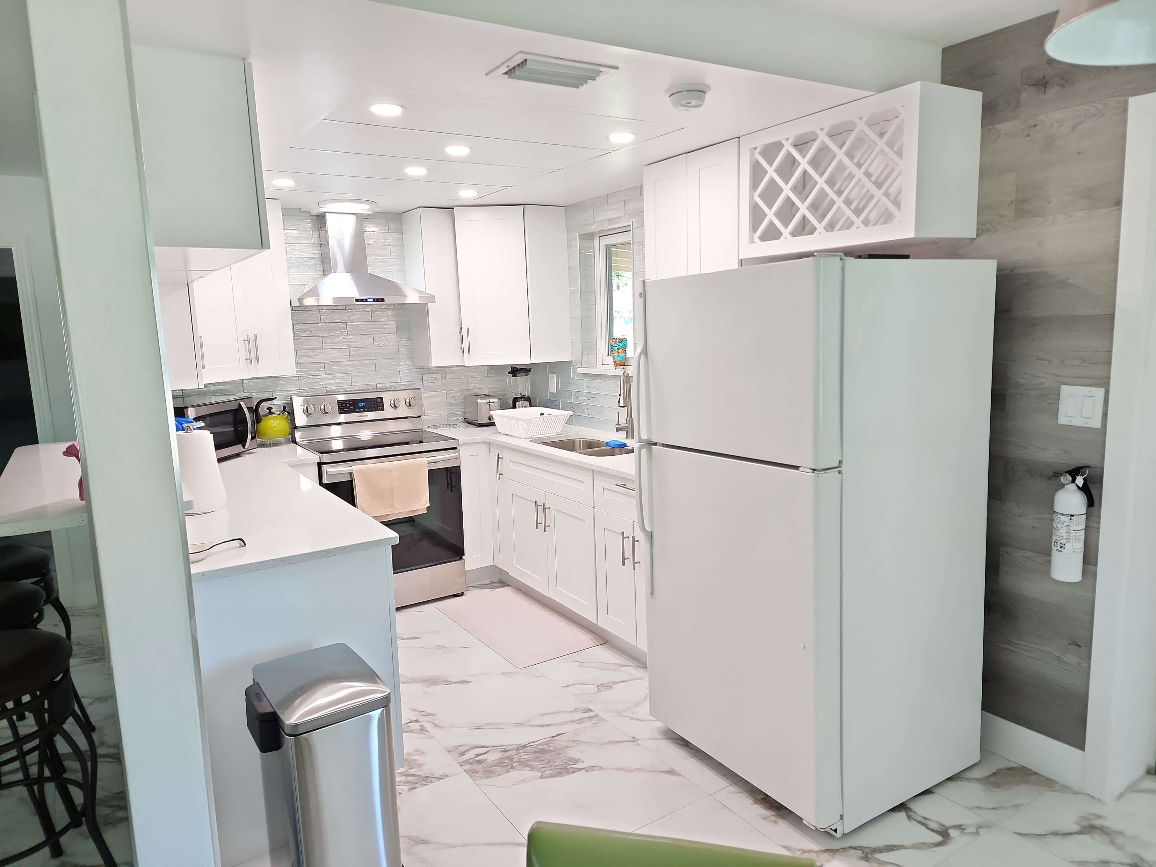 A modern kitchen with white cabinets, stainless steel appliances, and marble flooring.