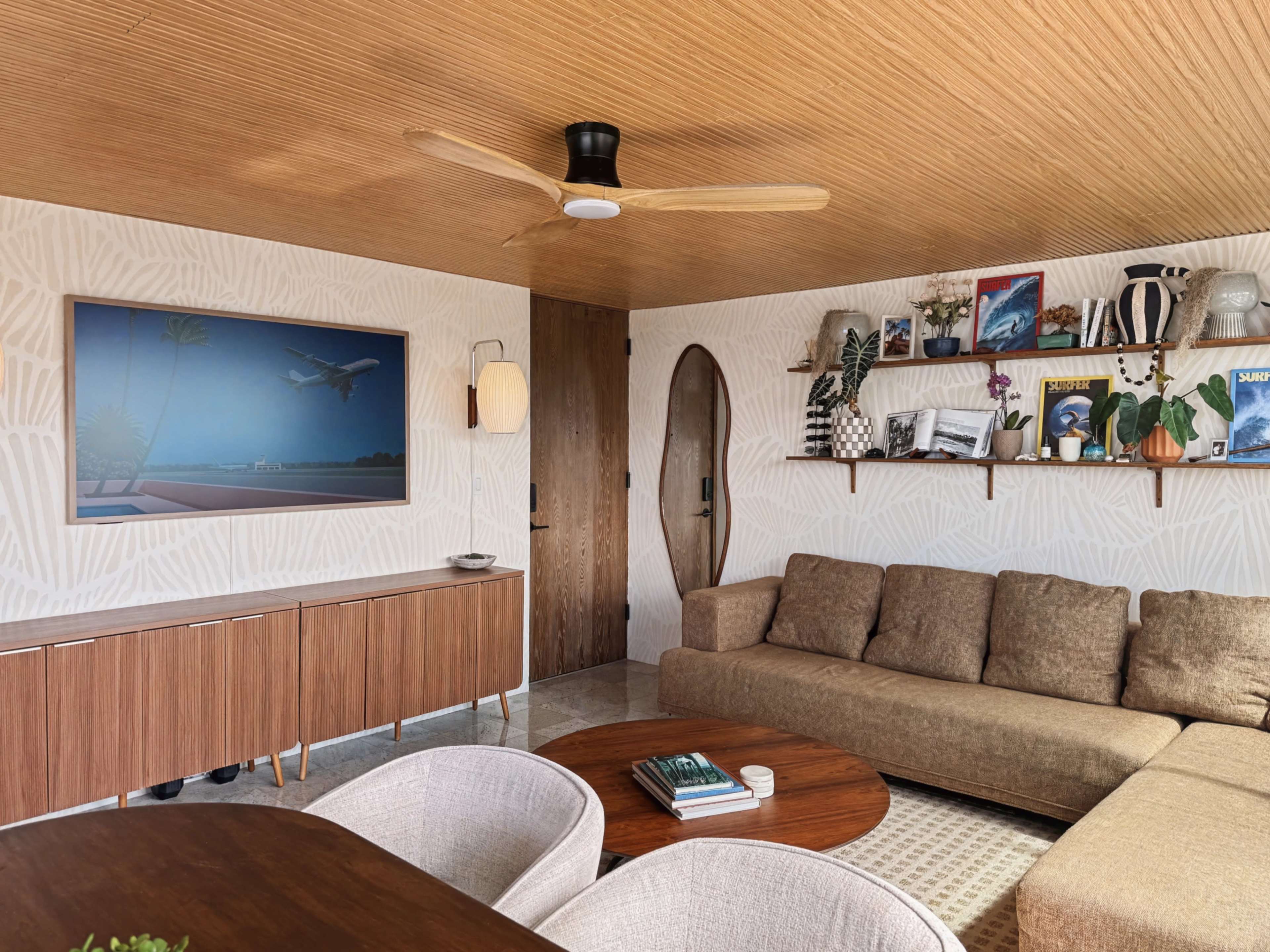 A modern living room features a large brown sectional sofa, a wooden coffee table, a wall-mounted shelf with décor items, and a striking plane-themed artwork.