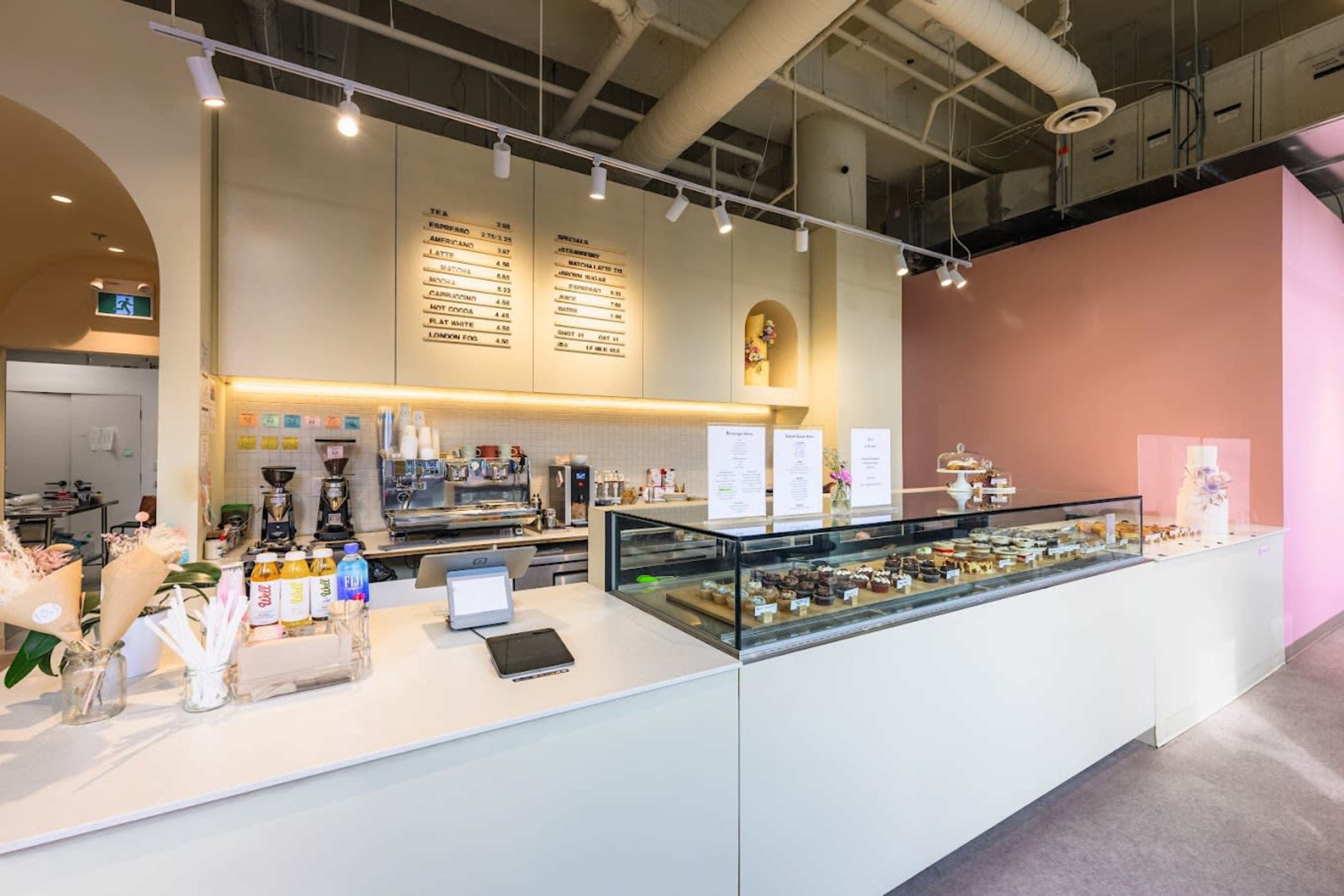 A modern café interior with a glass display case featuring various pastries and a counter with a coffee machine and menu board.