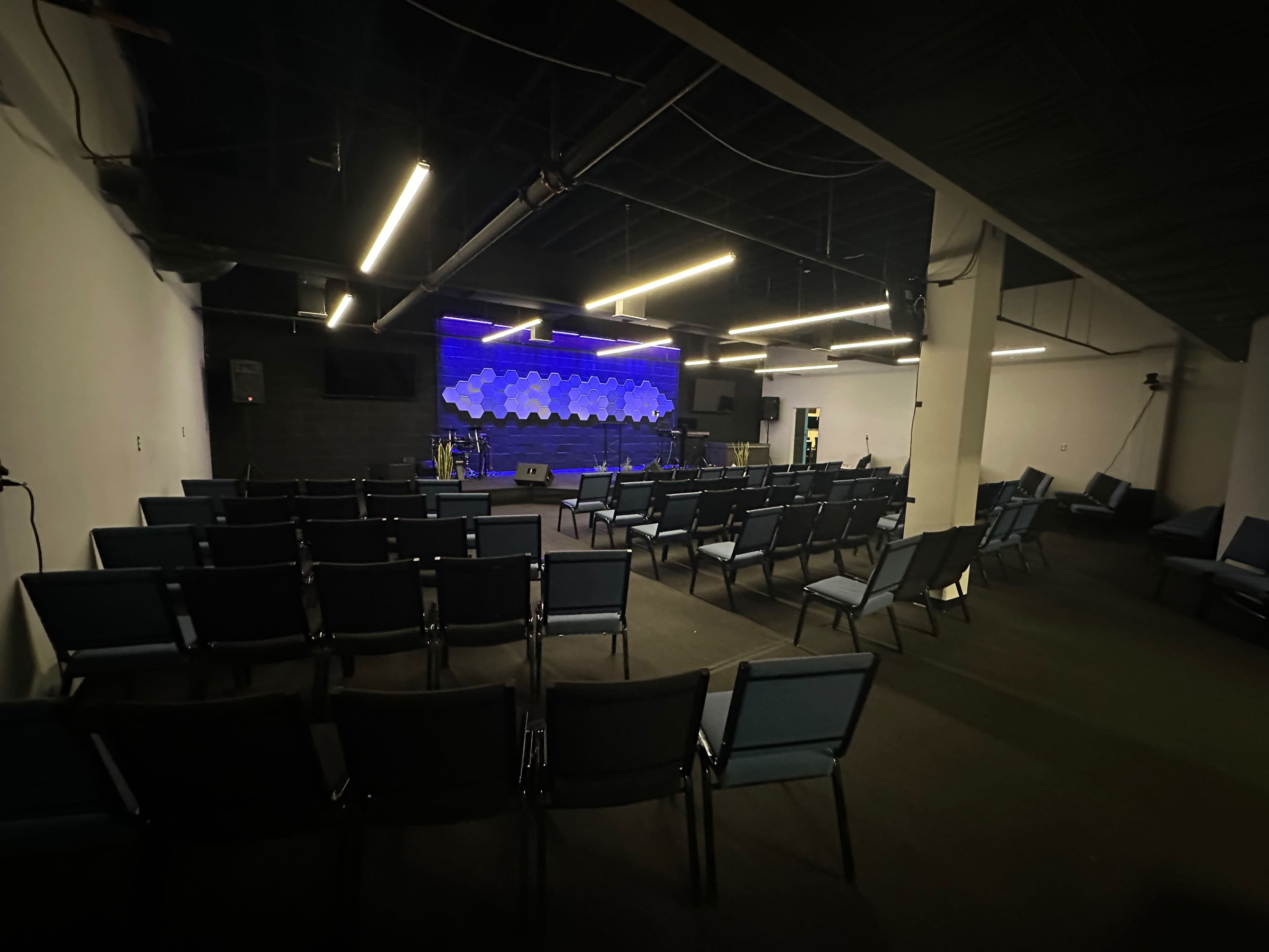 A spacious auditorium with rows of chairs facing a lit stage that features a decorative backdrop.