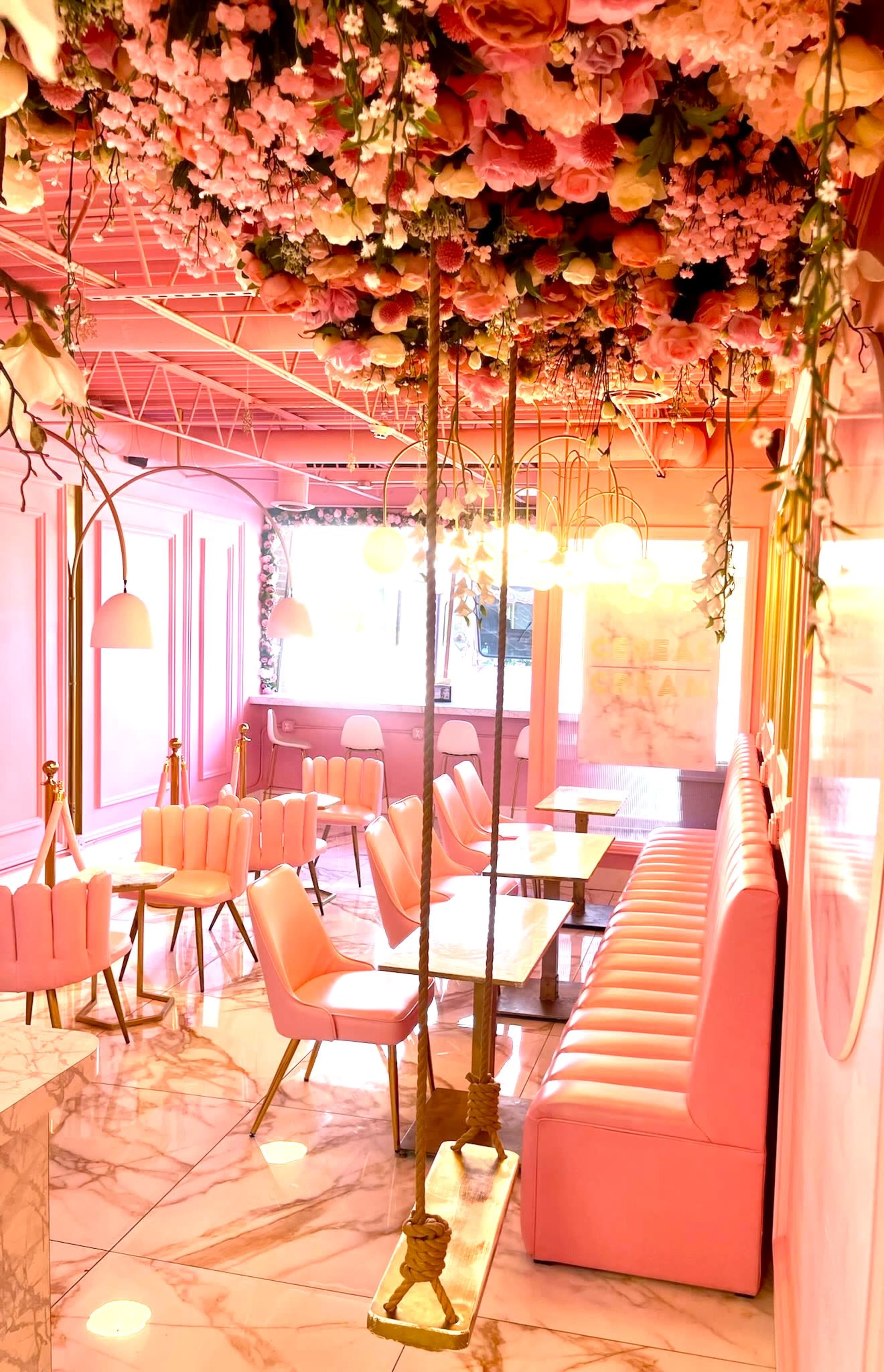 A pink-themed cafe interior with floral decorations on the ceiling, seating booths, and marble floors.