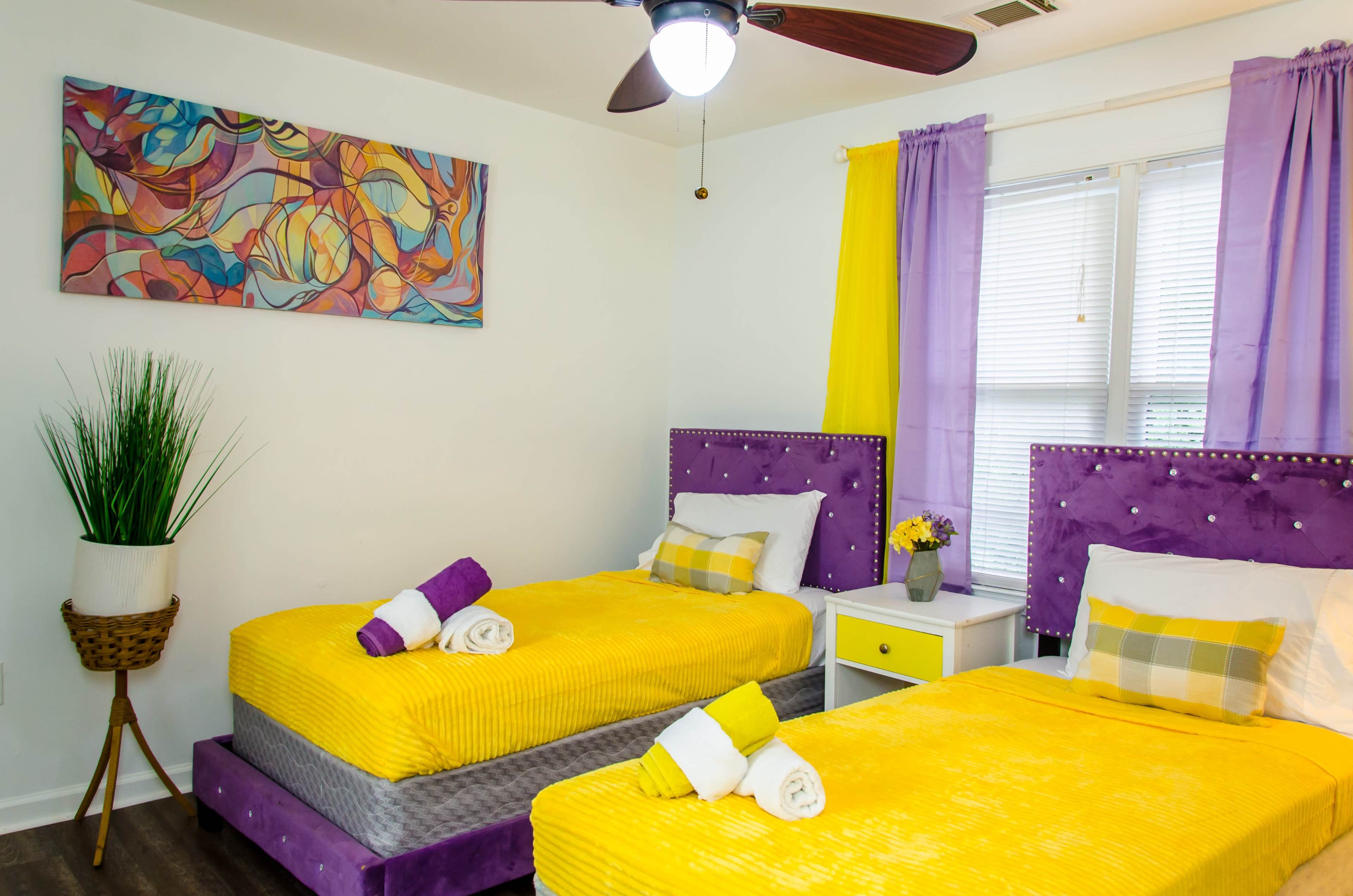 A brightly decorated bedroom with two yellow beds, purple headboards, and colorful wall art.