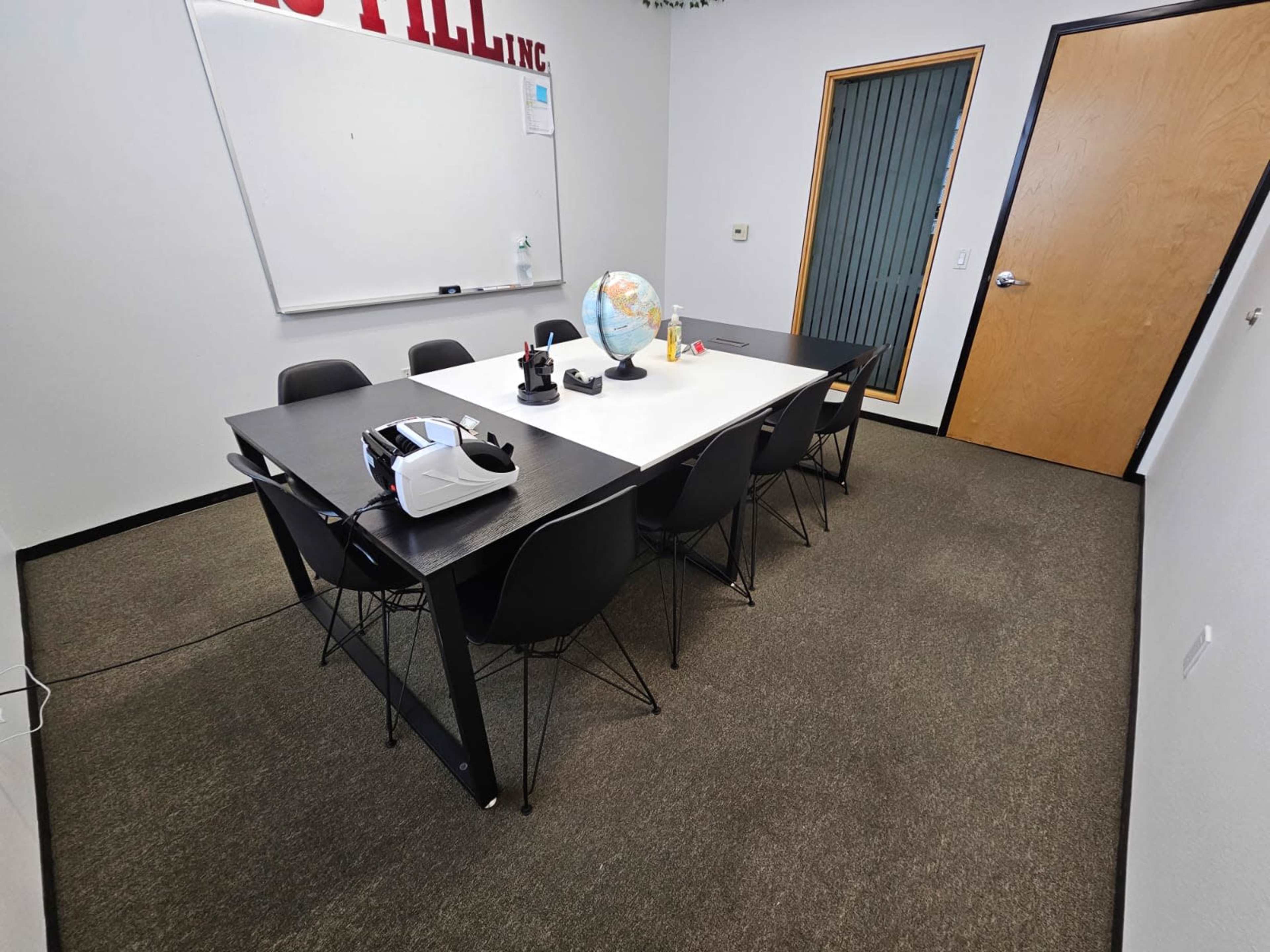 A conference room with a large table, several black chairs, a globe on the table, and a whiteboard on the wall.
