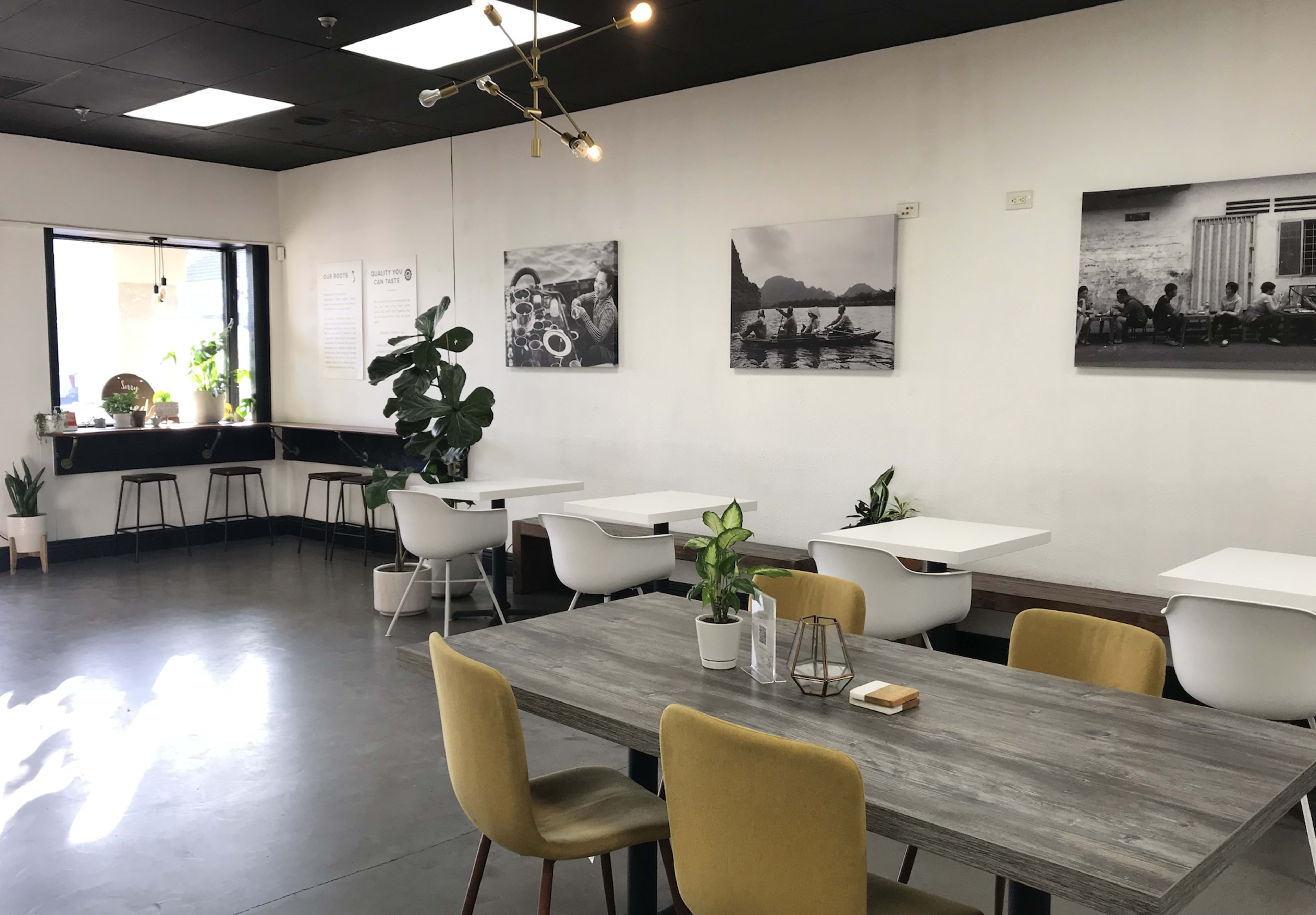 A modern café interior with several tables, plants, and framed photographs on the walls.