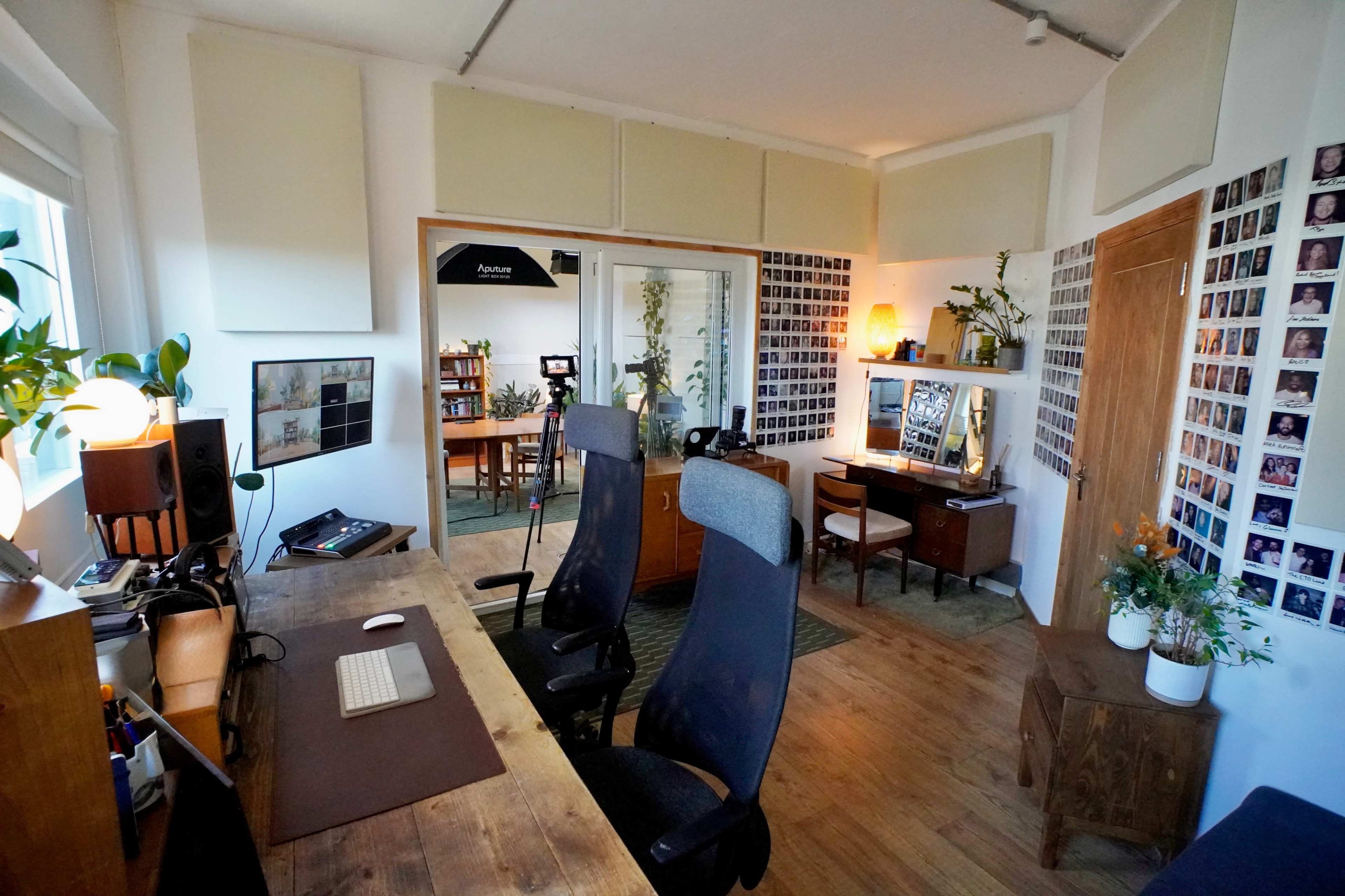 The image shows a cozy office space with wooden furniture, two ergonomic chairs, and walls adorned with numerous small photographs.