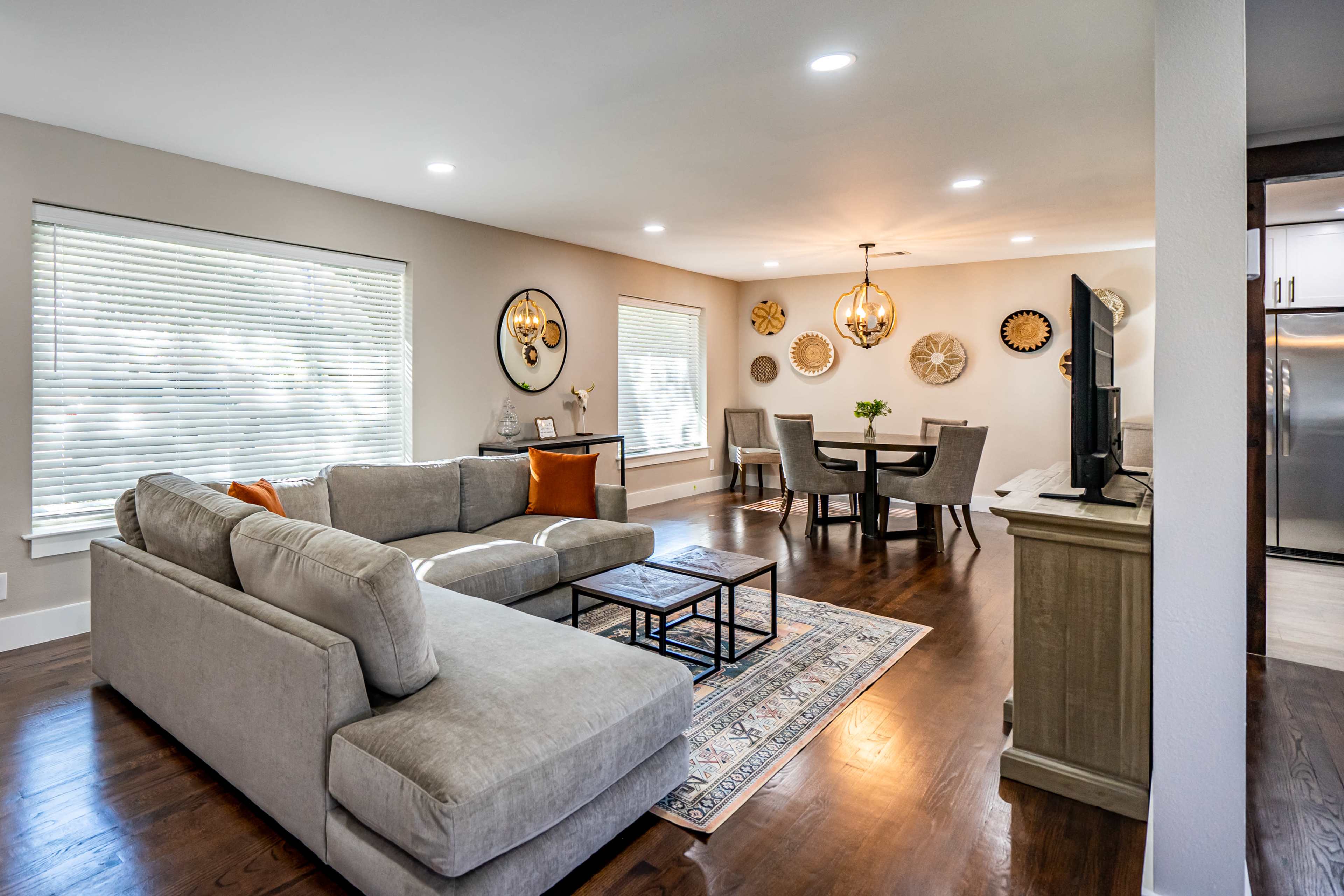 A modern living room and dining area featuring a gray sectional sofa, a round dining table with chairs, and decorative wall accents.