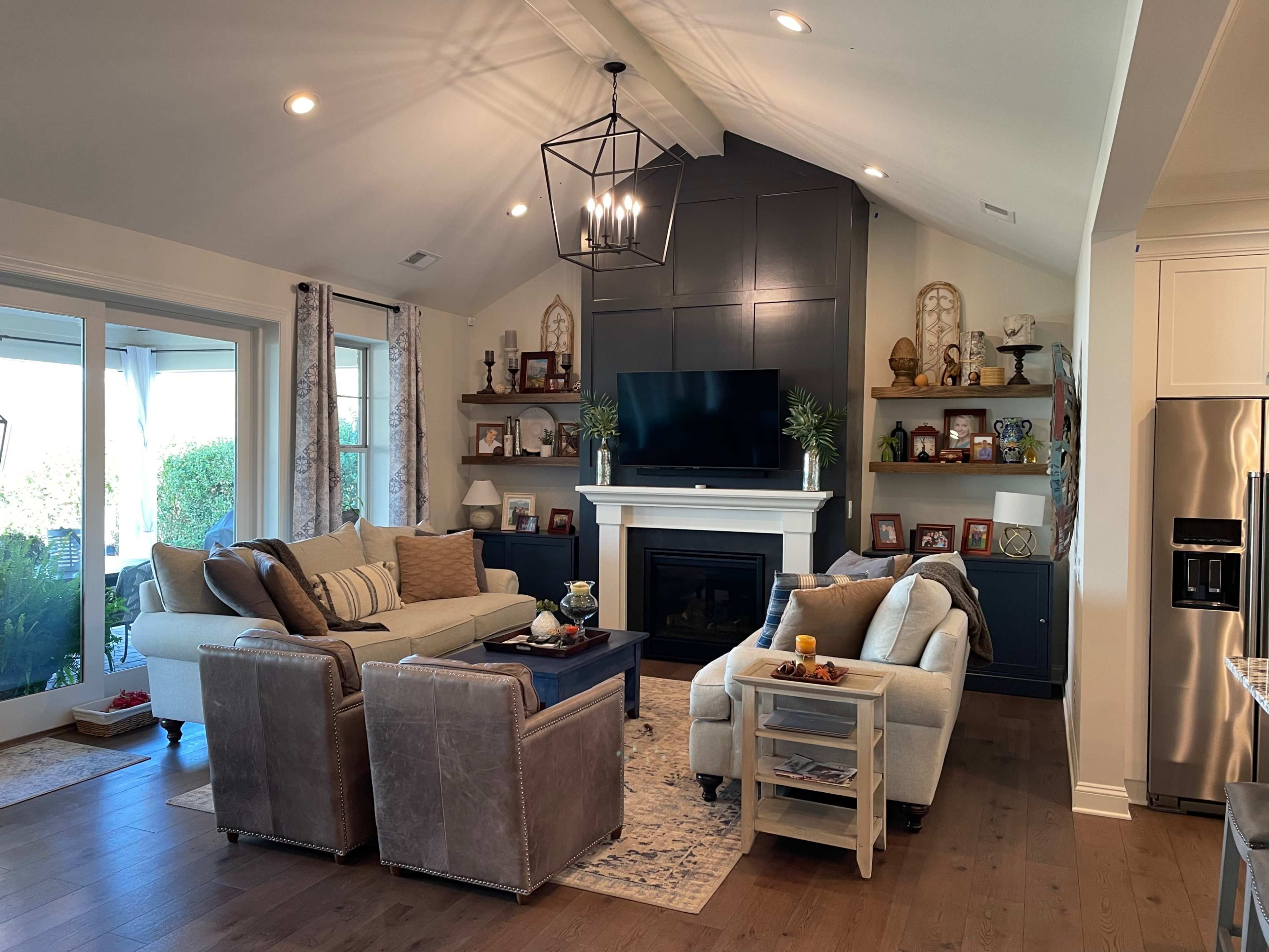 A cozy living room with two distinct seating areas, a fireplace, a large TV mounted on a dark wall, and shelves displaying various decorations.