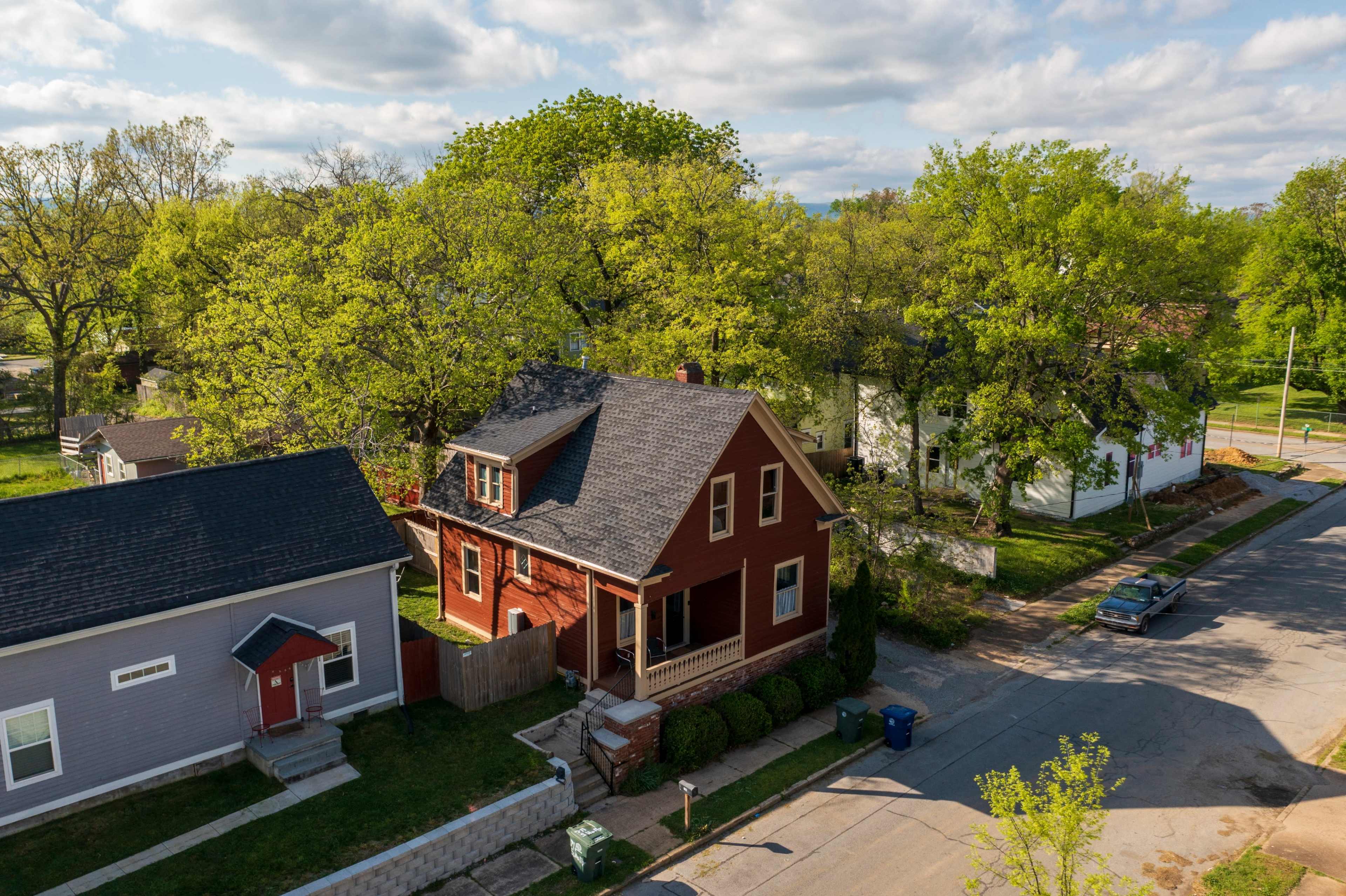 The image shows a residential neighborhood with a red house surrounded by green trees and a few other homes along a street.