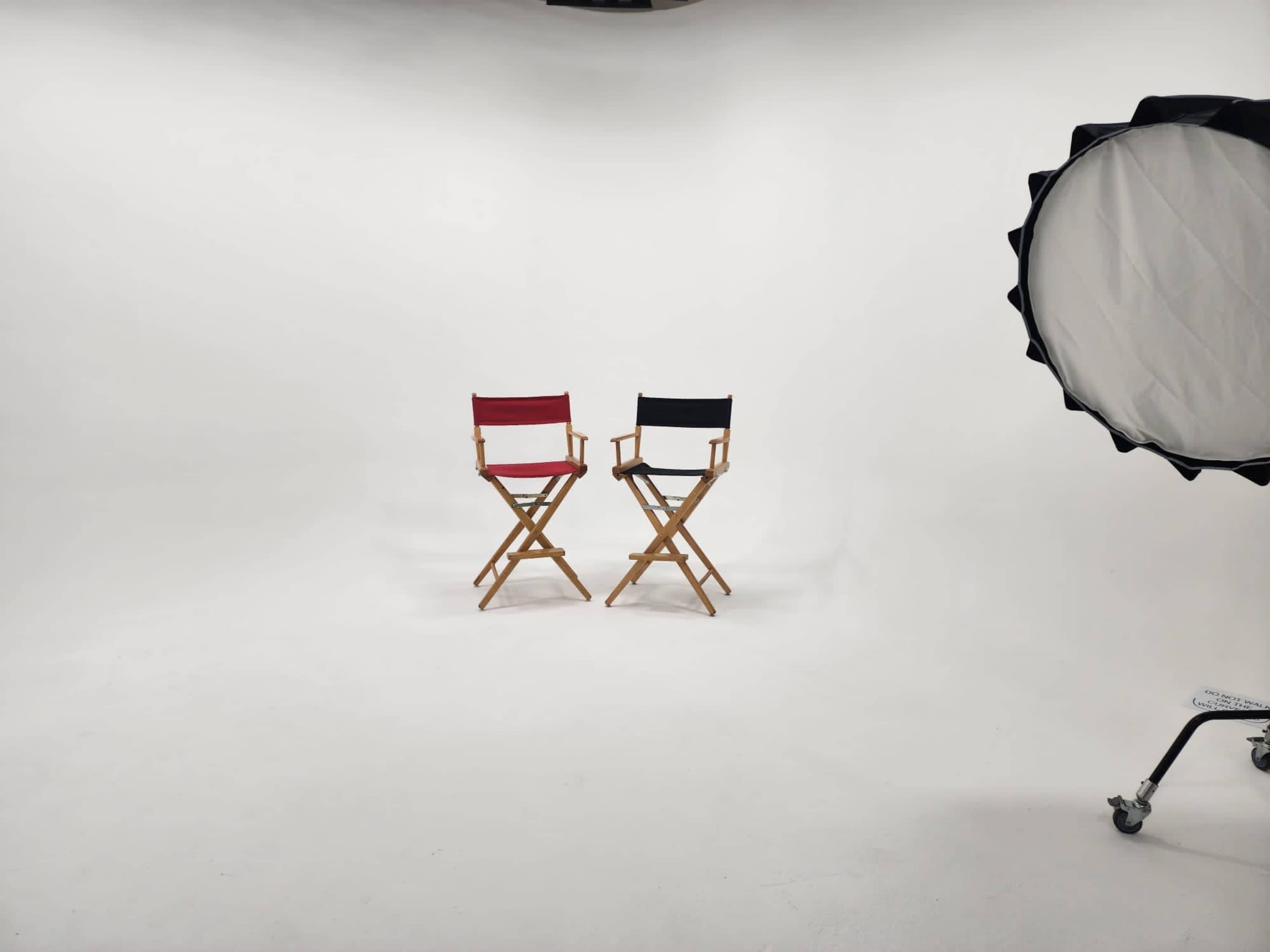 Two wooden director's chairs, one red and one black, positioned in a well-lit studio with a plain white background.