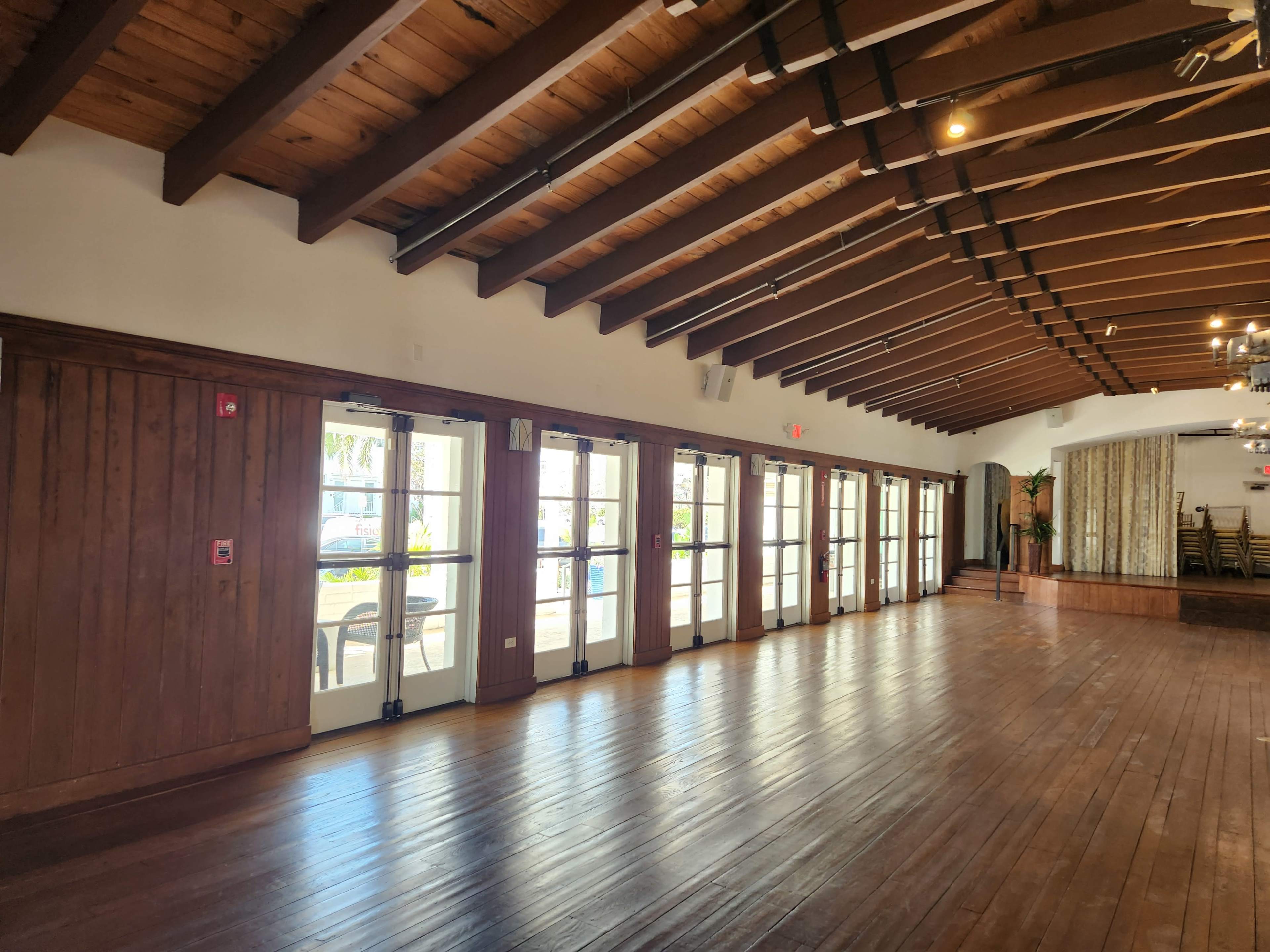 A spacious interior room with wooden beams and large glass doors leading to an outdoor area.