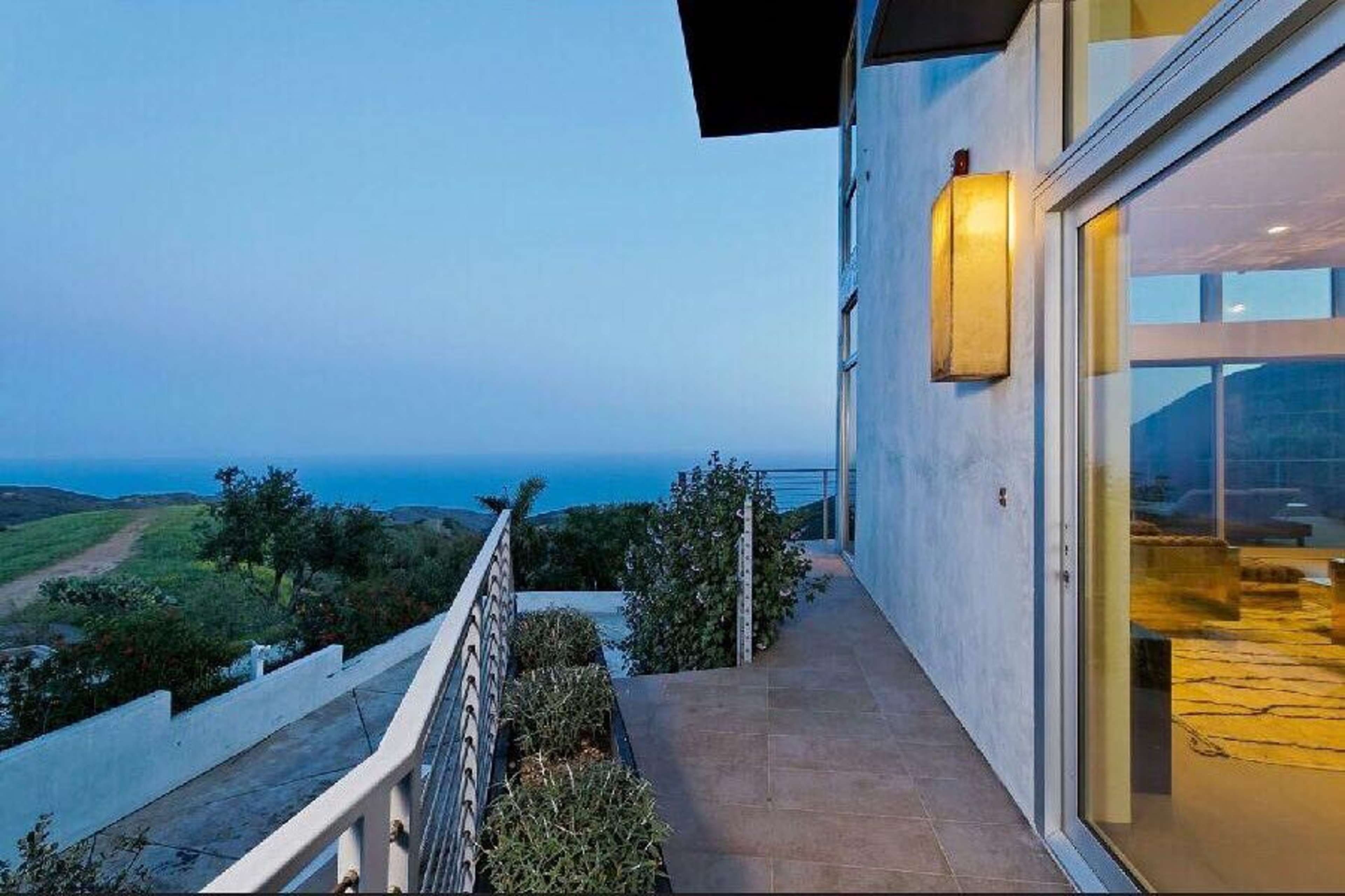 A modern home with large glass doors opening to a pathway overlooking a coastal view.