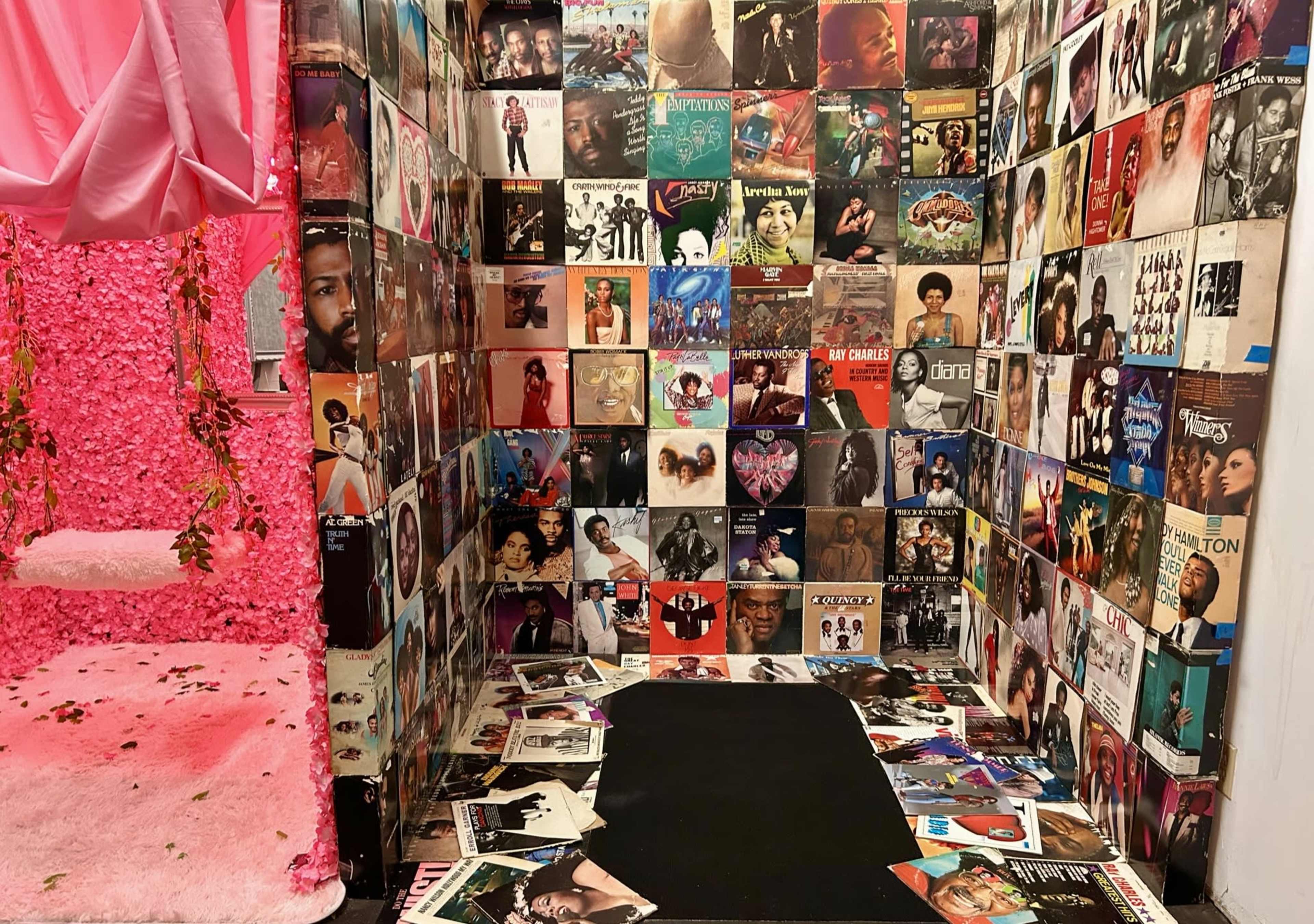 The scene features a corner adorned with colorful vinyl record covers lining the walls, surrounded by scattered album covers on the floor, with a pink, plush area and decorative flowers.