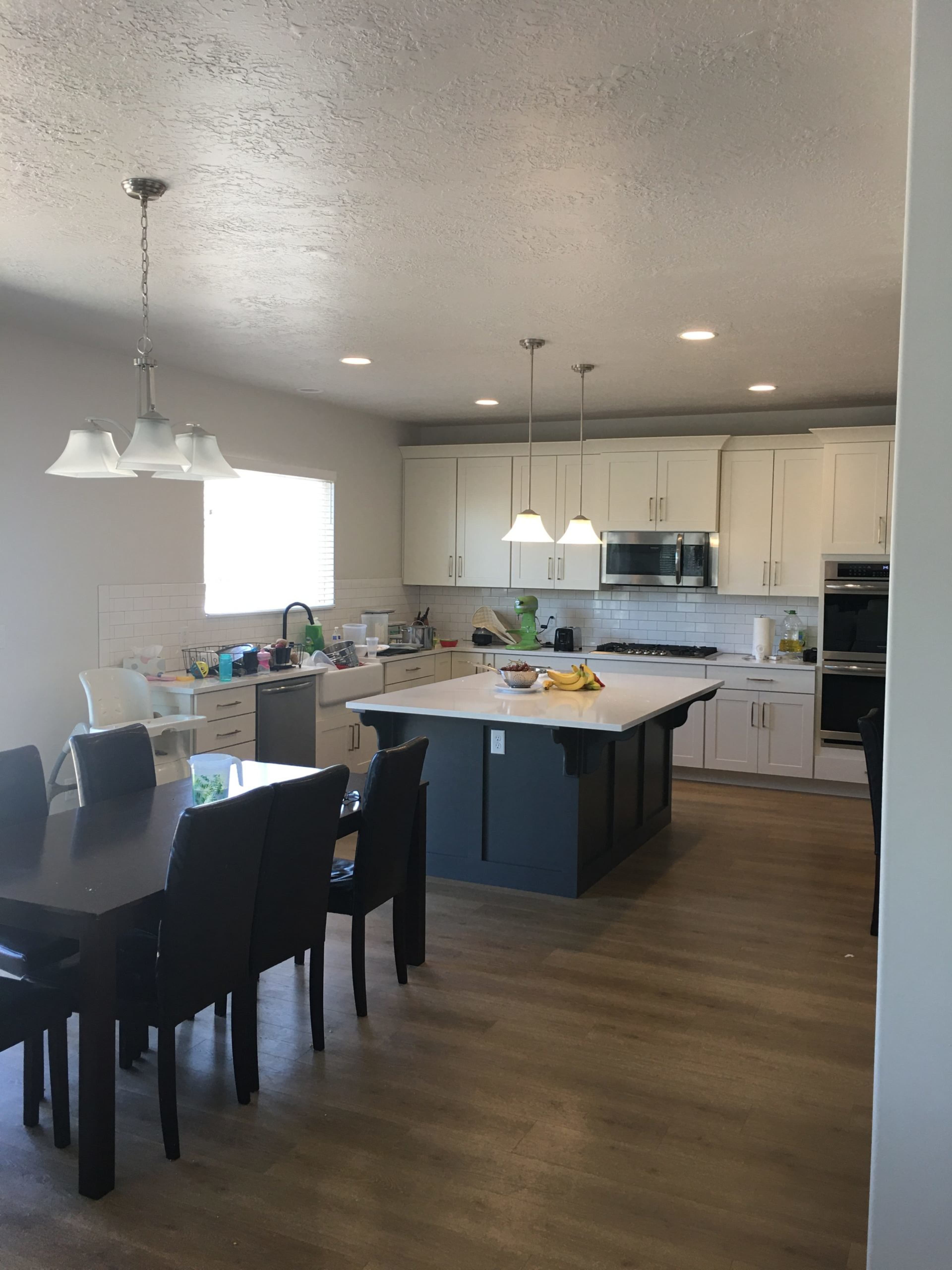 A modern kitchen features white cabinets, a central island, and a dining area with a dark wooden table and chairs.