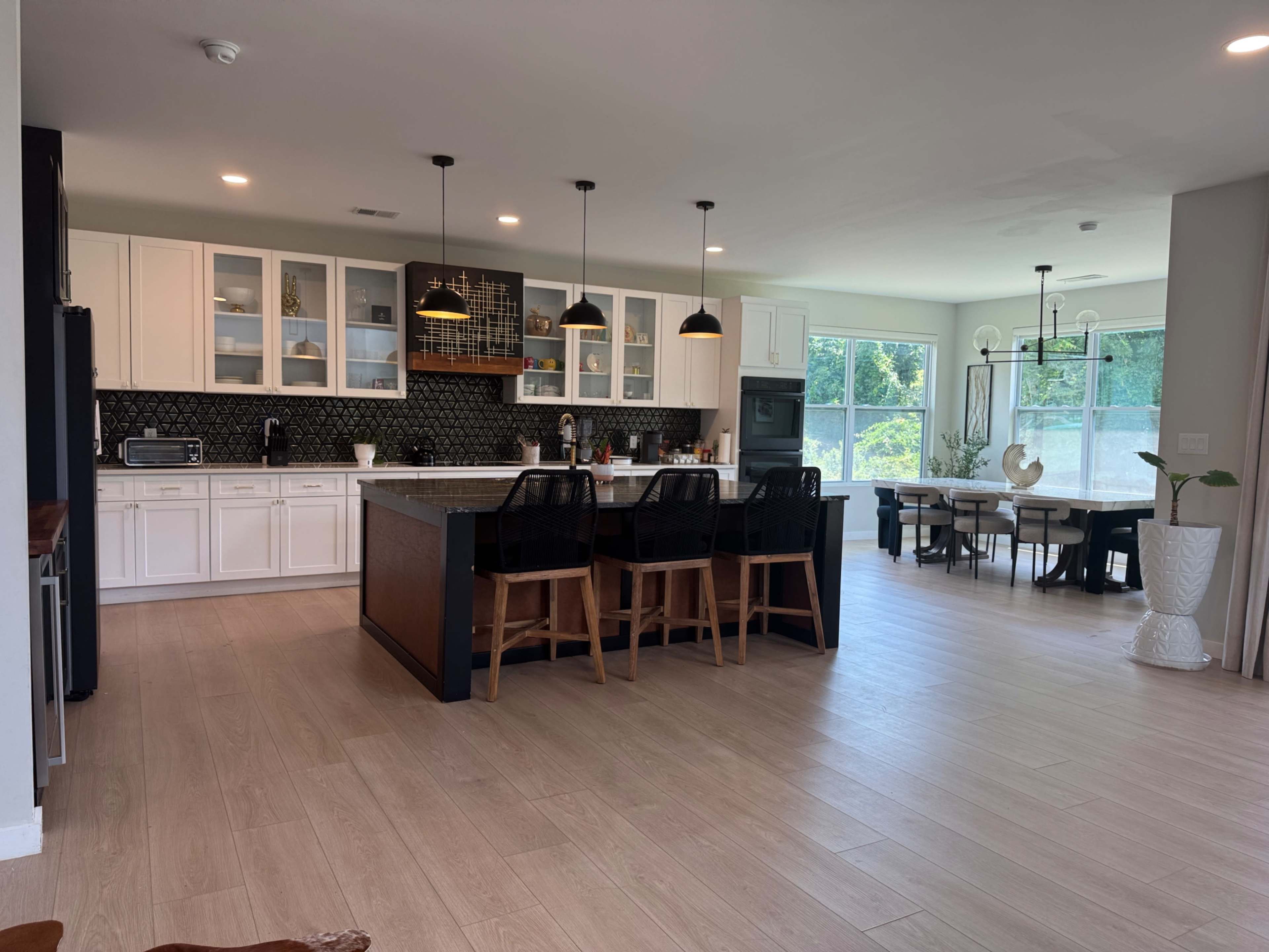 A modern kitchen features white cabinets, a large island with seating, and ample natural light from windows.
