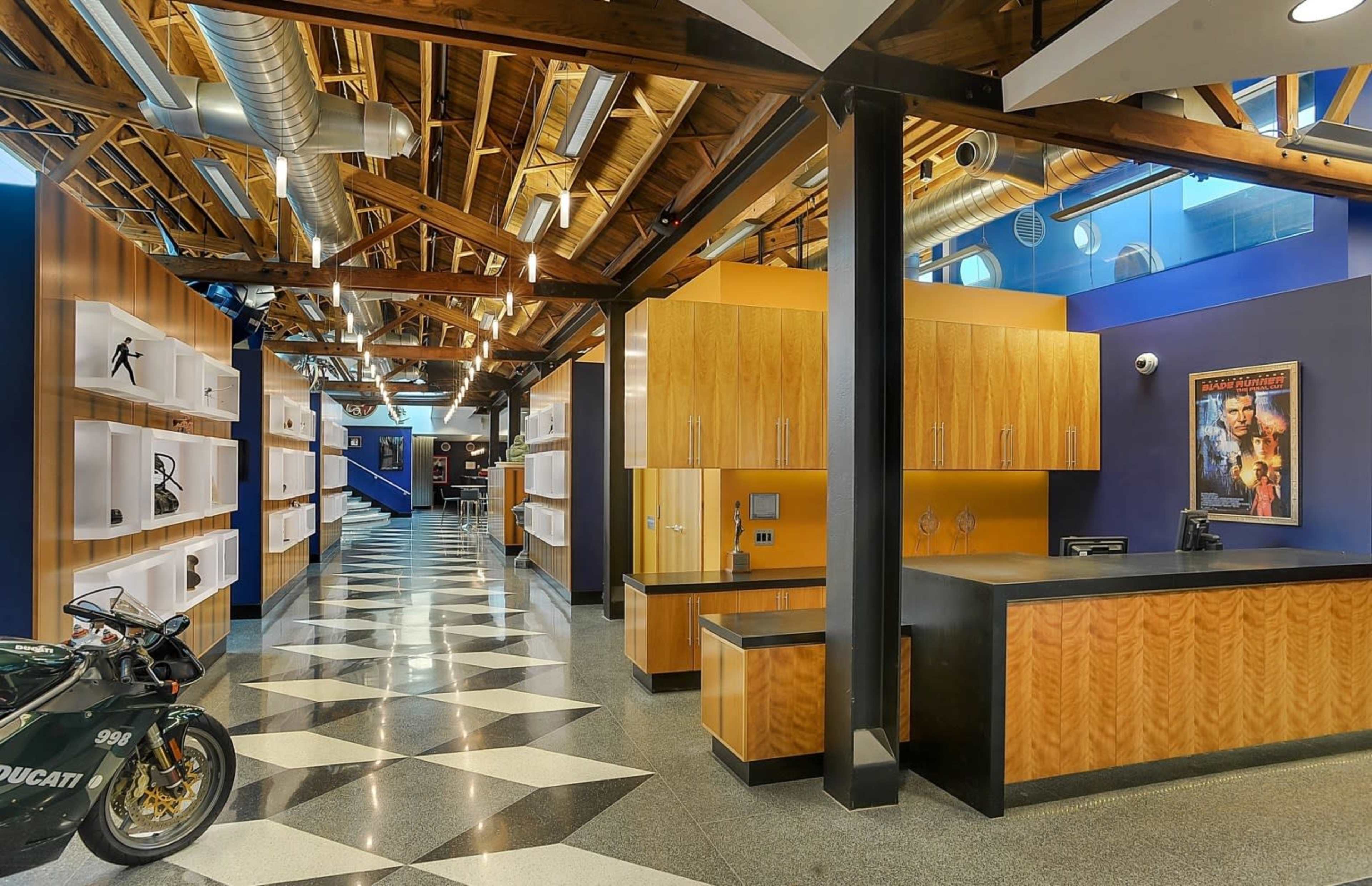 A modern interior space with a checkered floor, wooden beams, and a reception area featuring a motorcycle and illuminated display shelves.