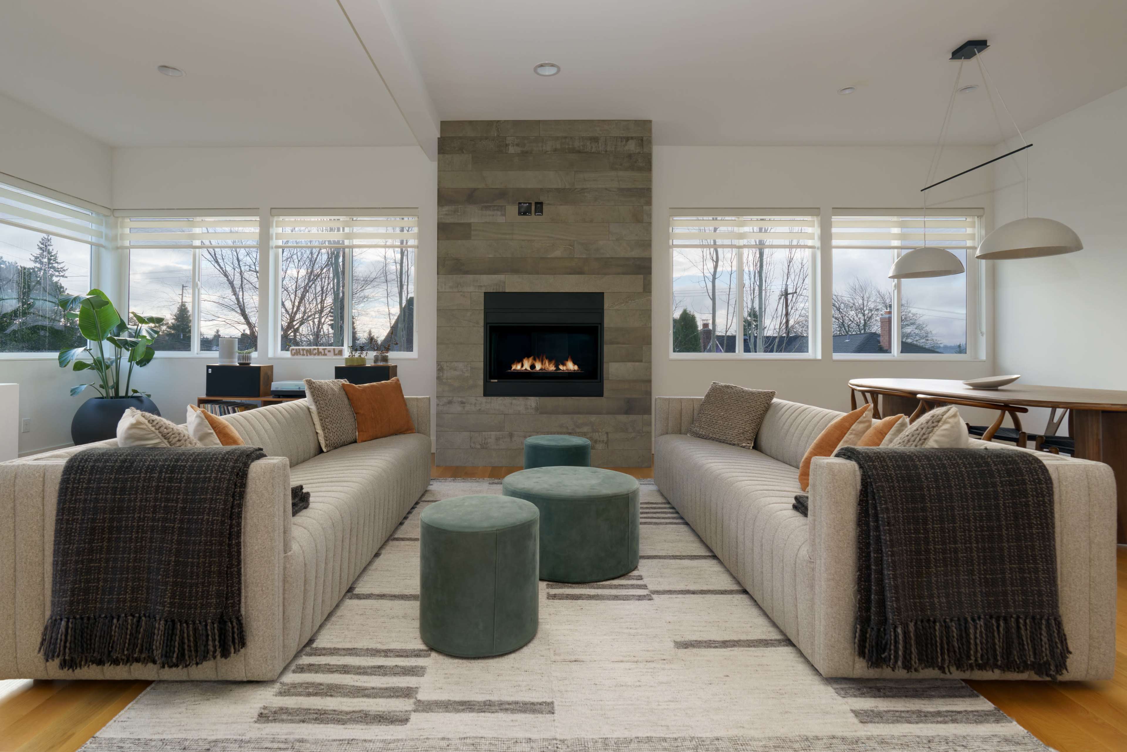 A modern living room with two sofas facing each other, a fireplace in the center wall, and a dining area visible in the background.