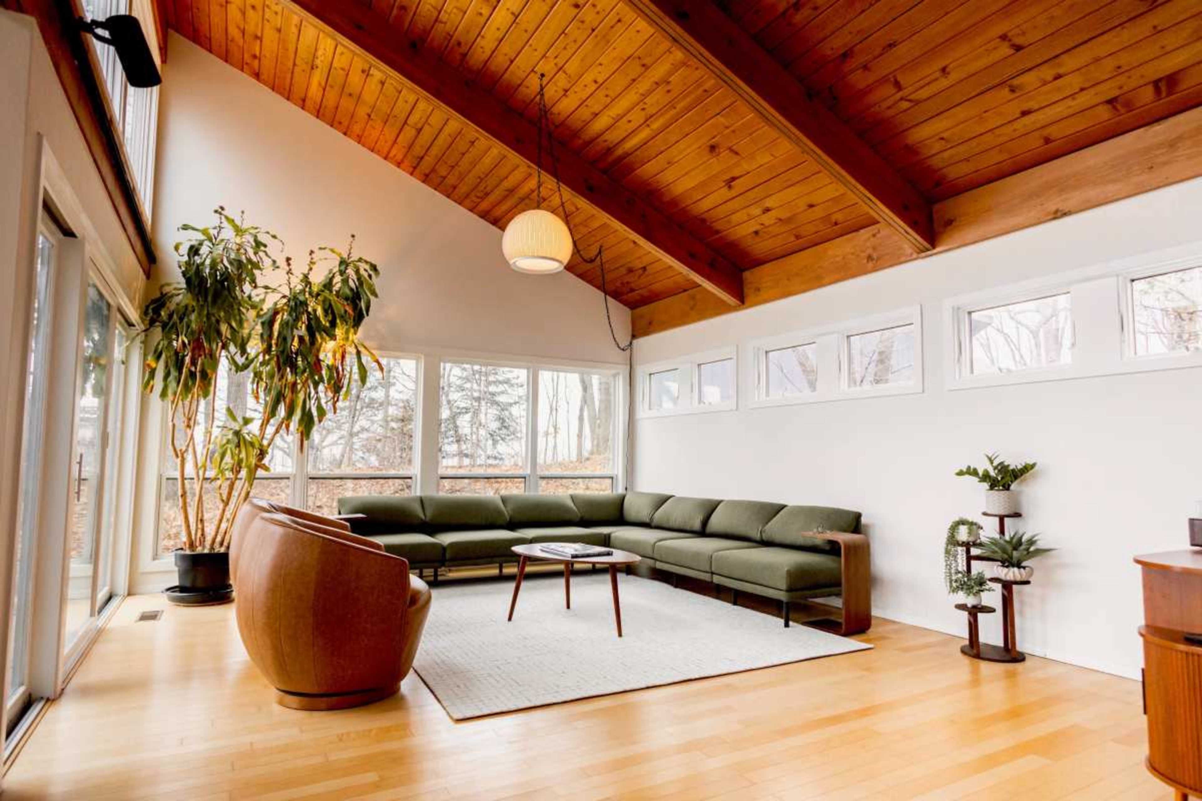 A spacious living room features a green sectional sofa, a round coffee table, and large windows that allow natural light to fill the space.