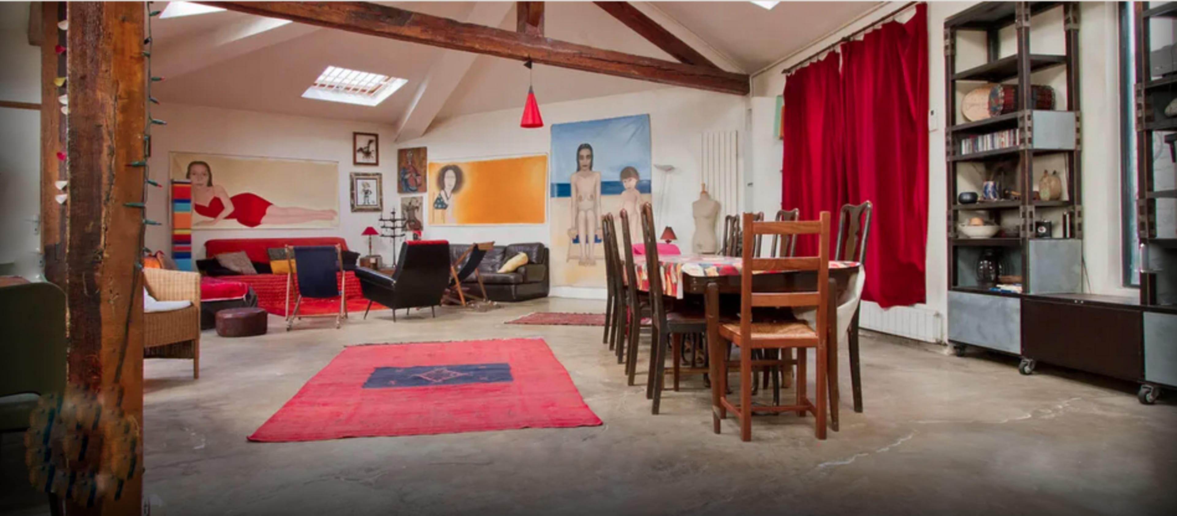 A spacious, open living area with a dining table, various seating options, and colorful artwork on the walls.