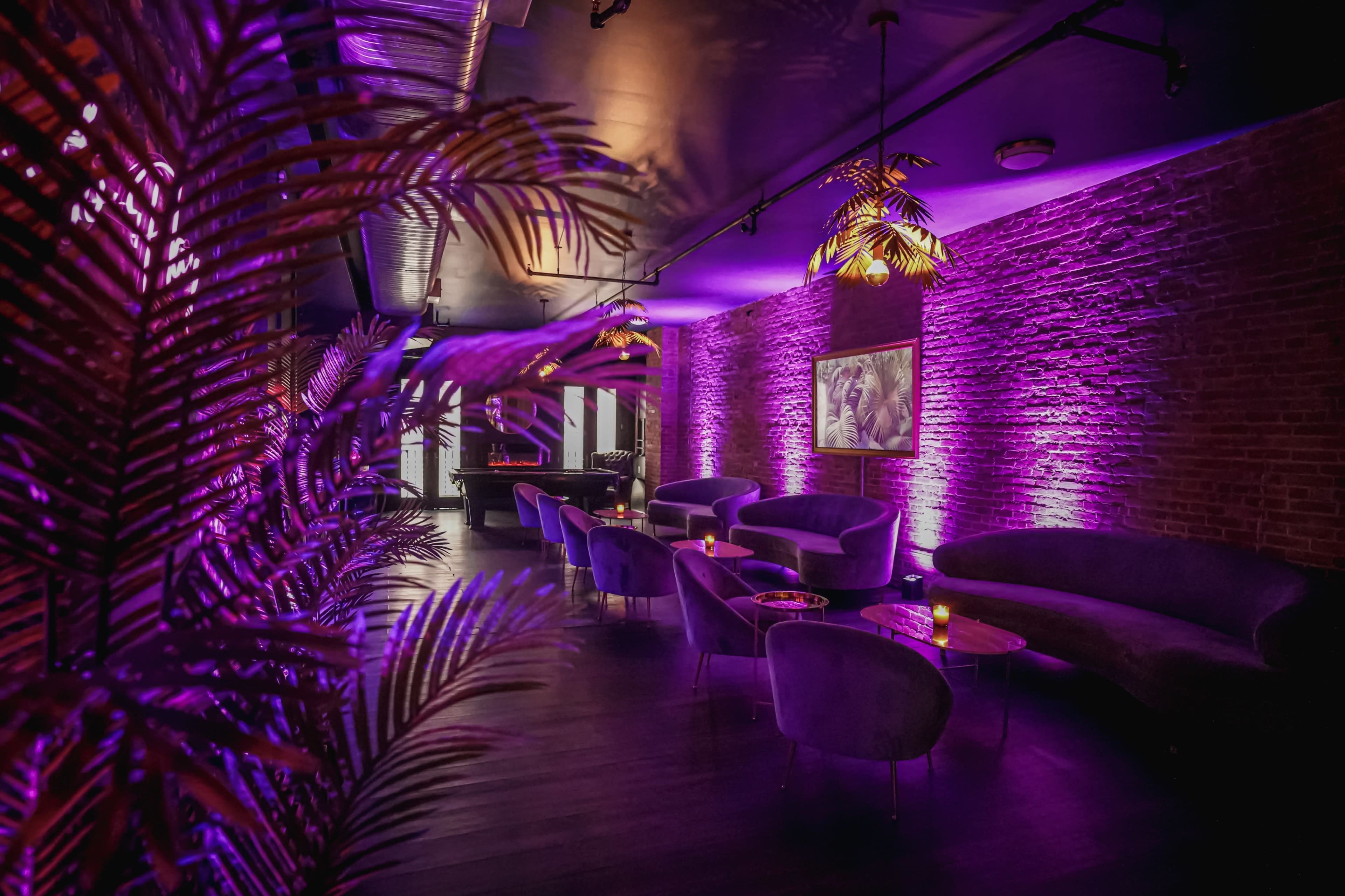 A lounge area features purple-lit walls, plush seating, and decorative plants, creating an intimate atmosphere.