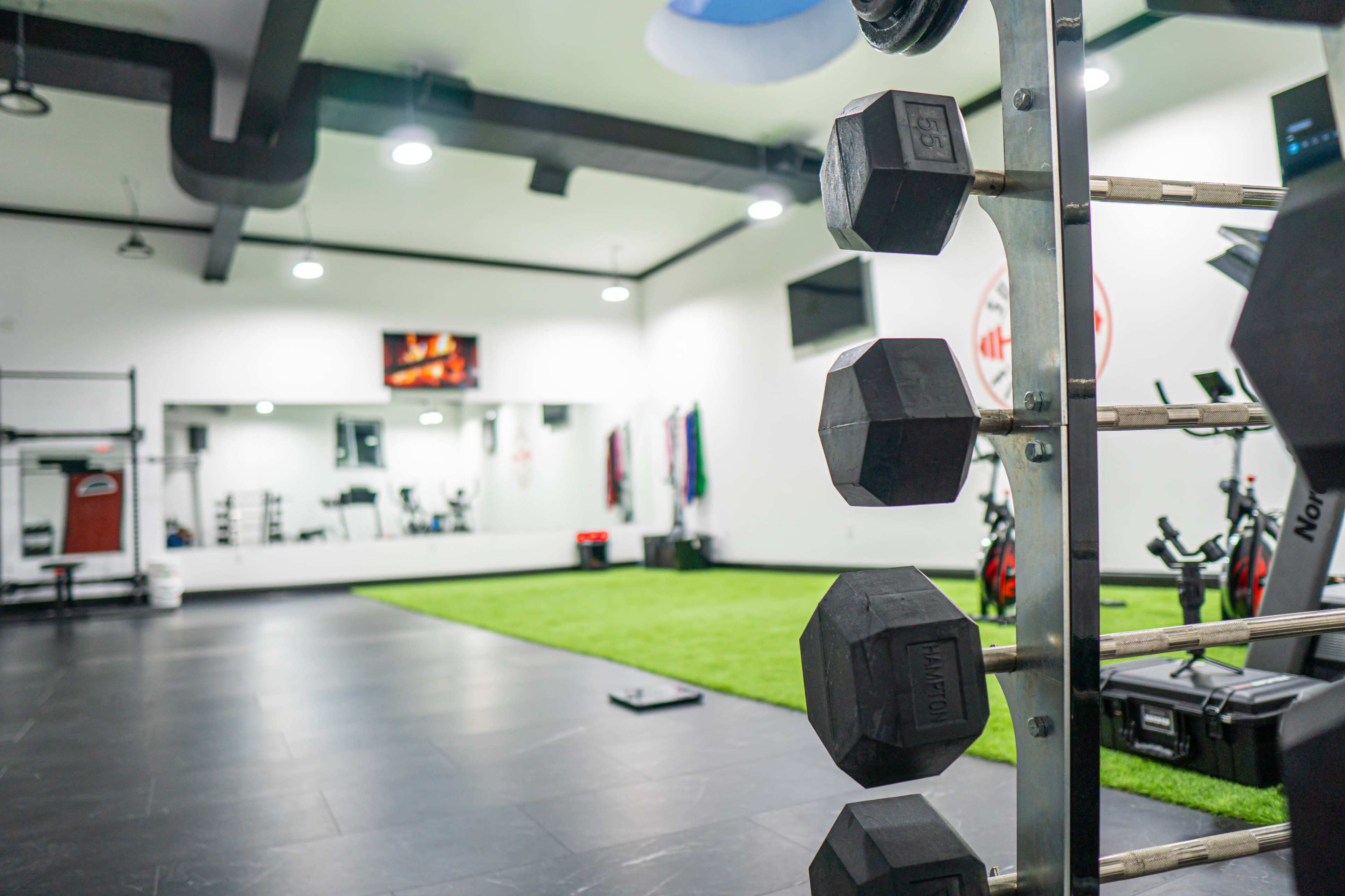 A fitness center with a rack of dumbbells in the foreground and exercise equipment in the background.