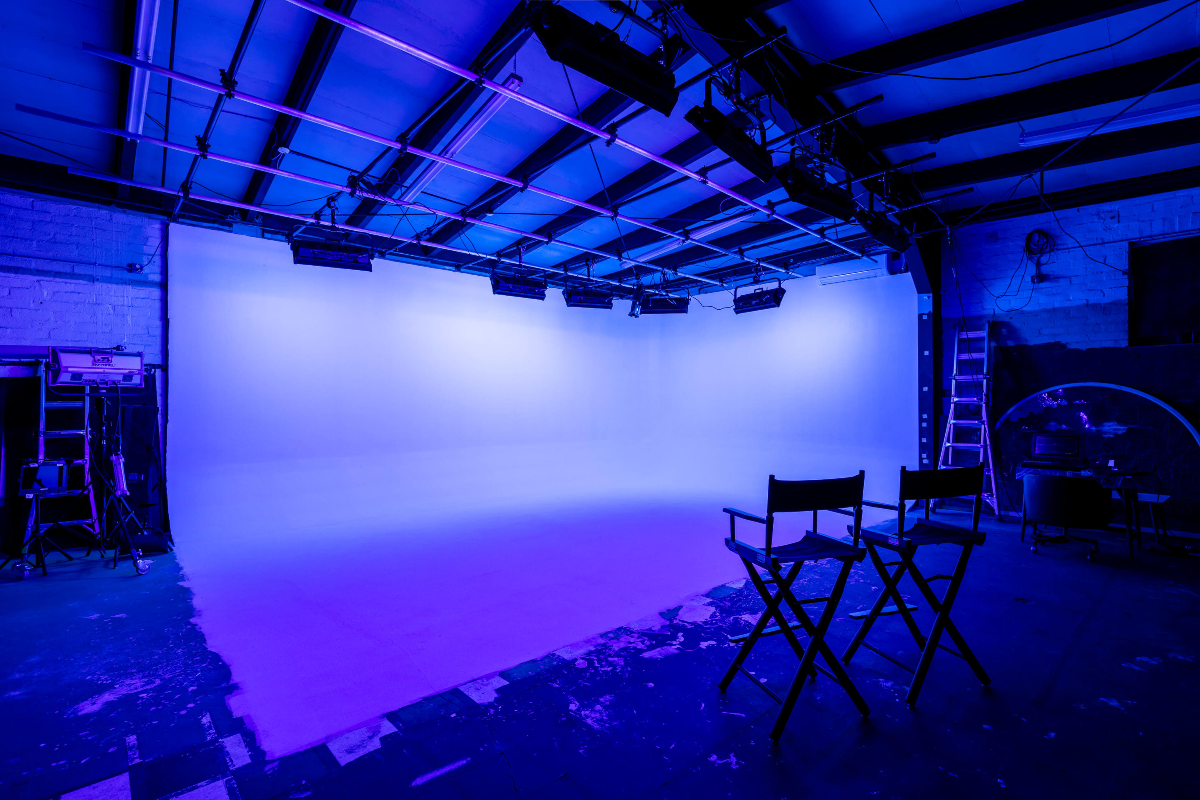 A photography studio with a blue-lit backdrop, two director's chairs, and lighting equipment mounted on the ceiling.