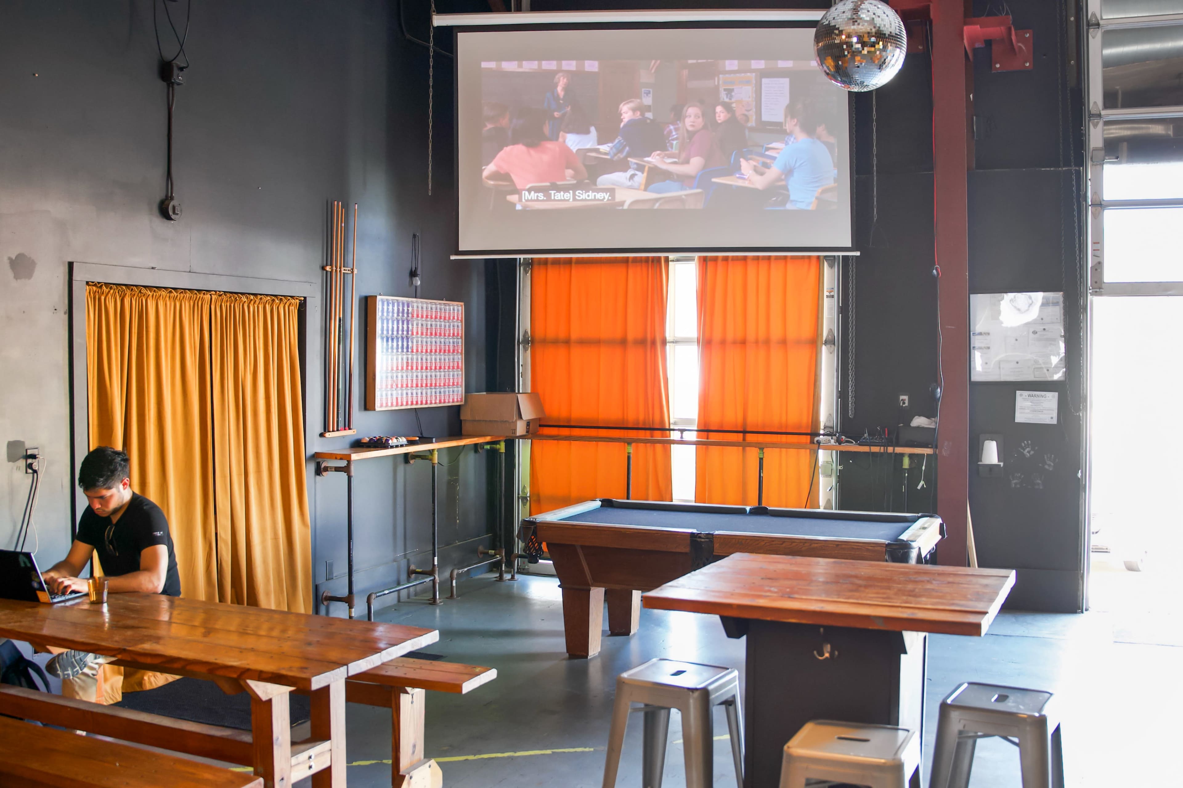 A classroom scene is projected on a screen in a dimly lit room featuring wooden tables and a pool table.