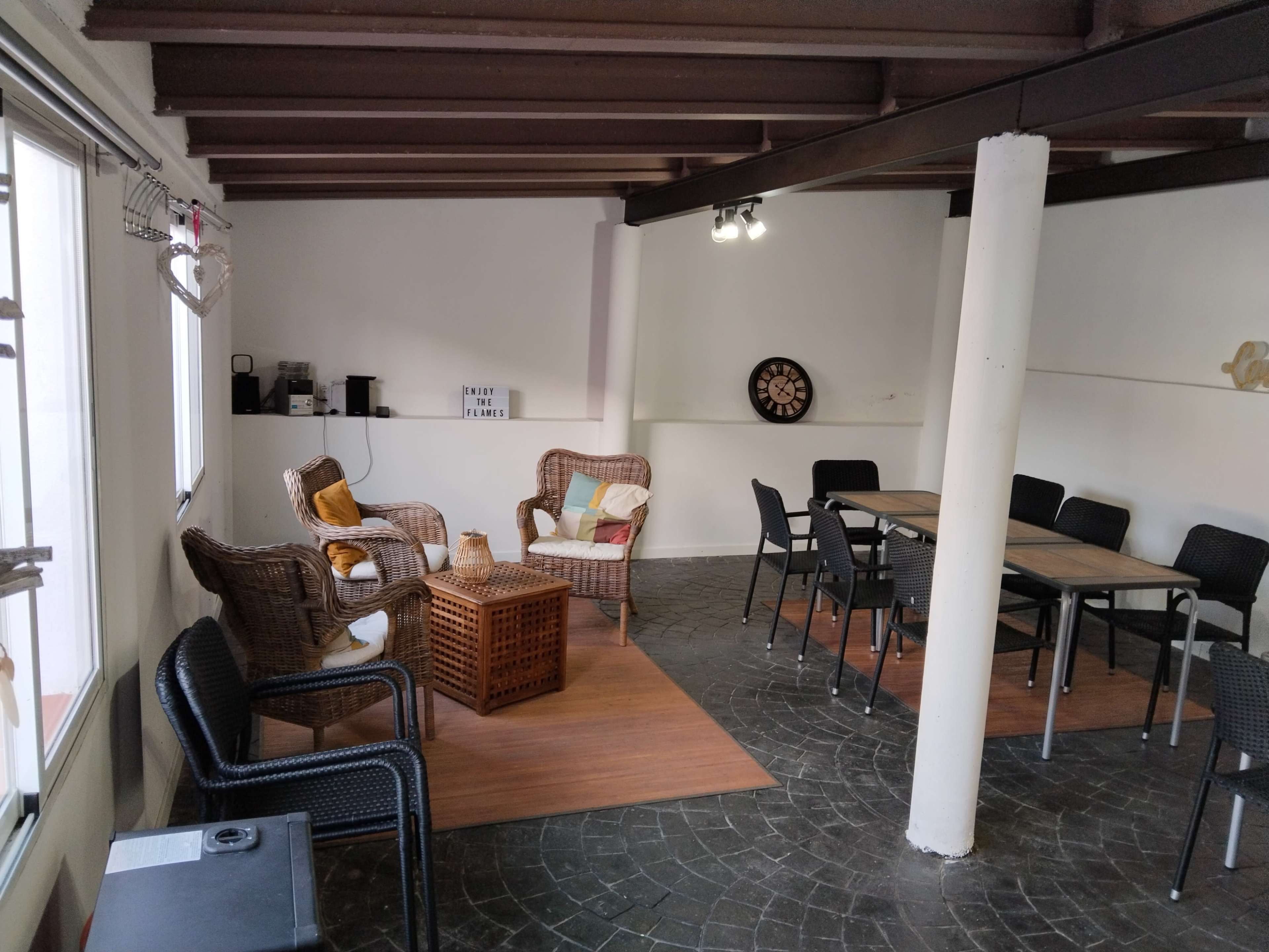 The image shows a spacious room with two wicker chairs and a coffee table on one side, and a dining table with black chairs on the other side.
