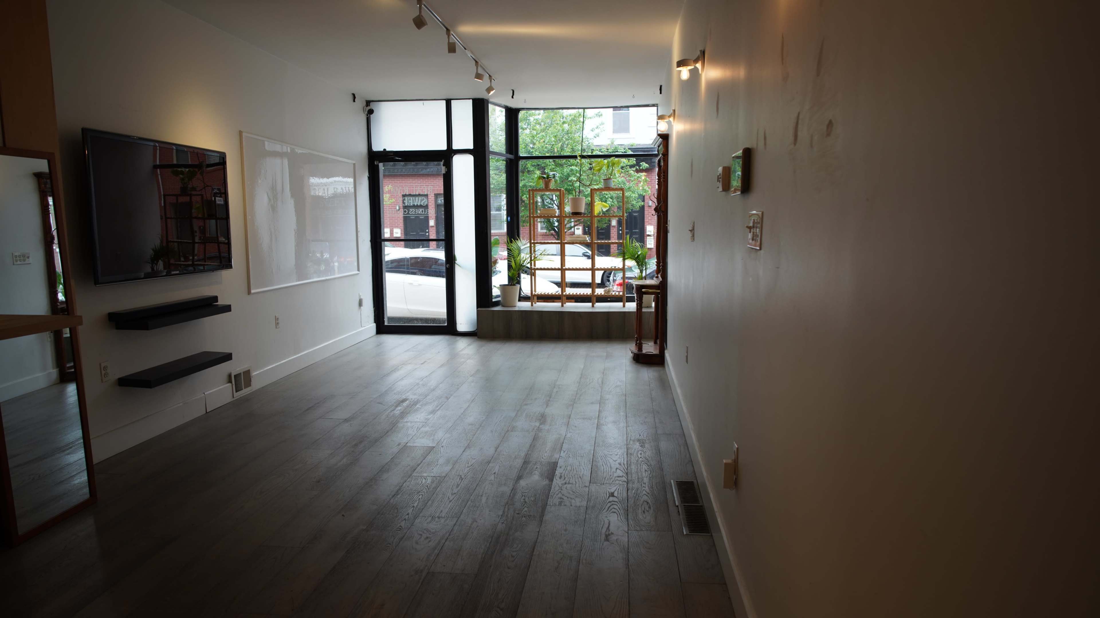 The interior of a modern, unfinished commercial space features wooden flooring, large windows displaying a street view, and minimal furnishings.