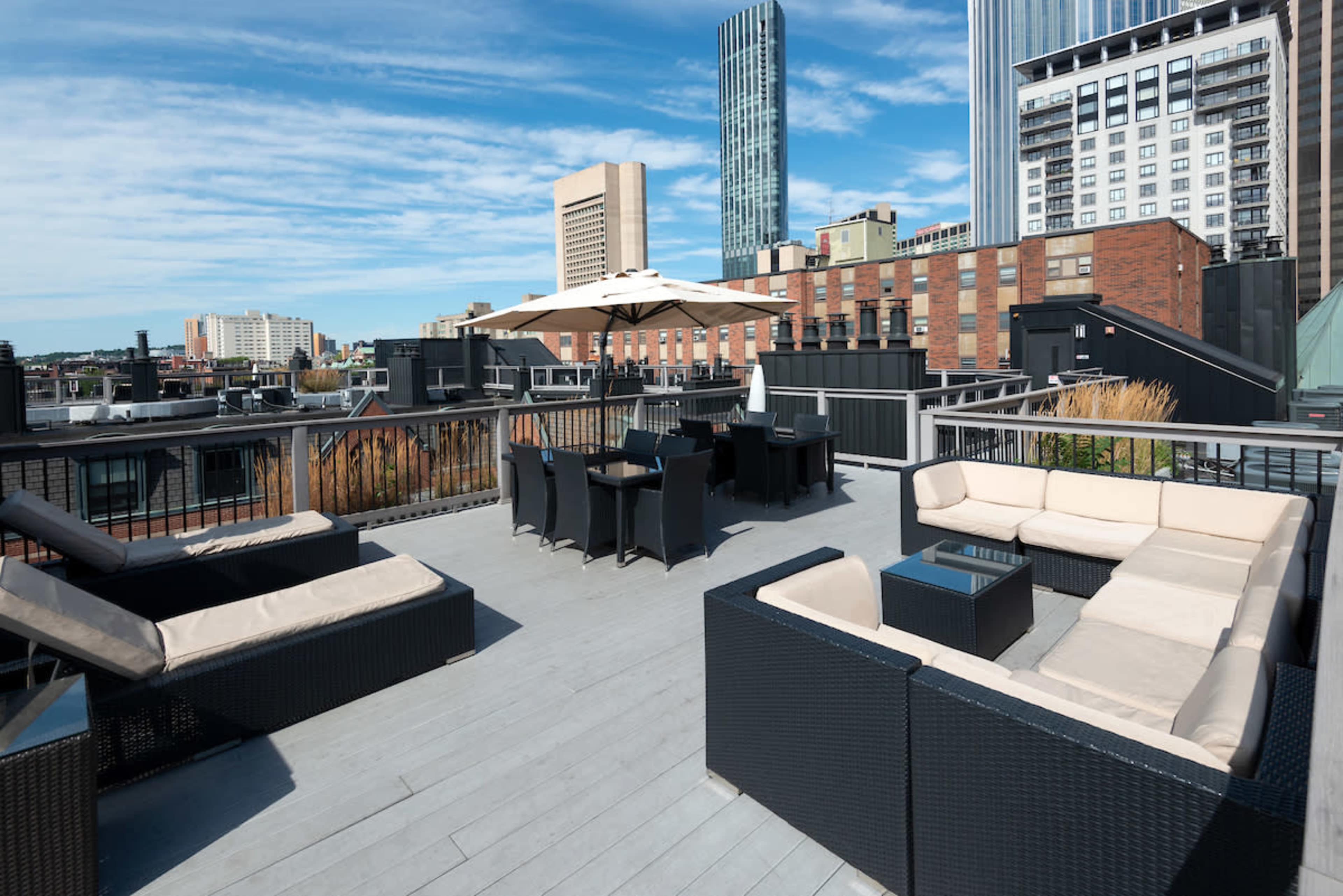 The rooftop features modern outdoor furniture, including a sectional sofa and dining set, with city buildings visible in the background.