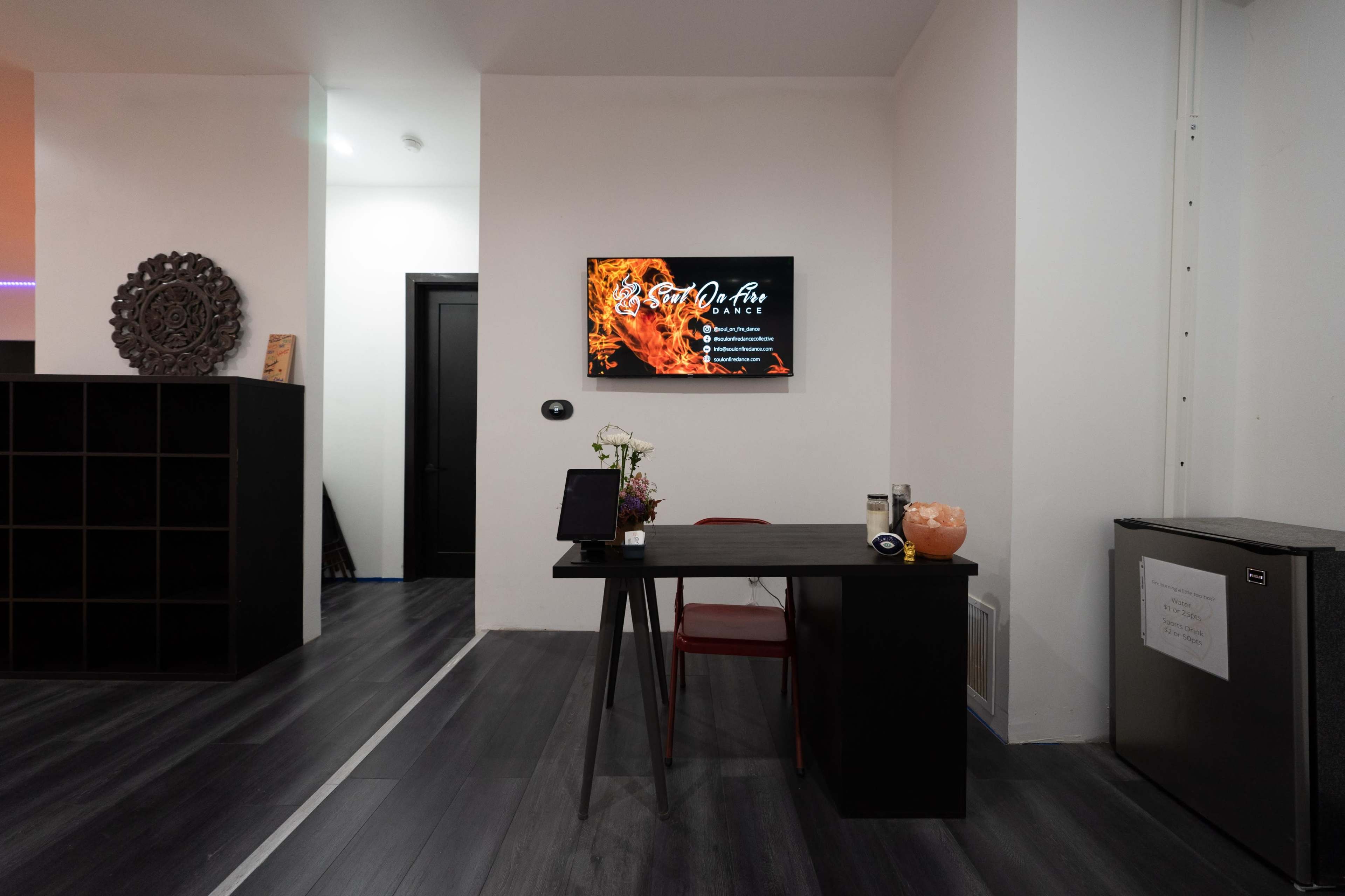 A modern reception area featuring a desk with a flower vase, a TV mounted on the wall displaying digital content, and a black shelving unit.