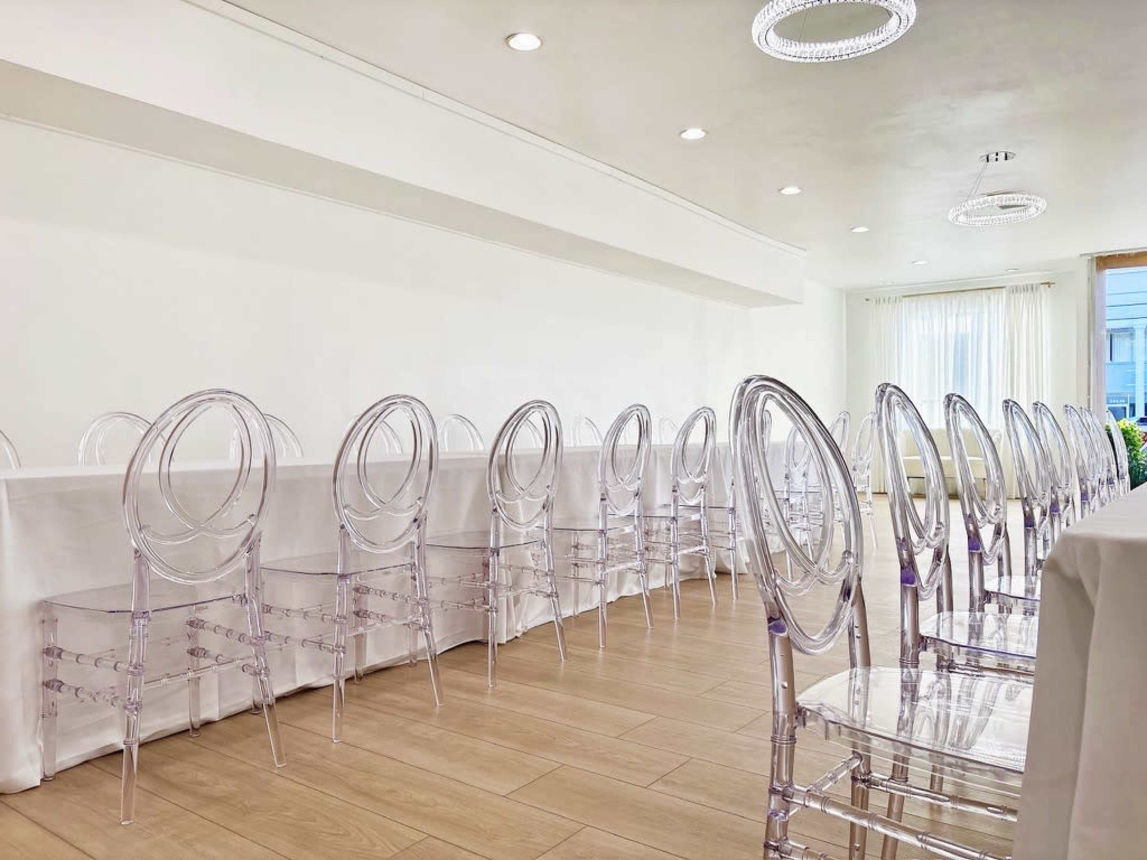 A long table set for a formal gathering is surrounded by clear acrylic chairs in a well-lit room.