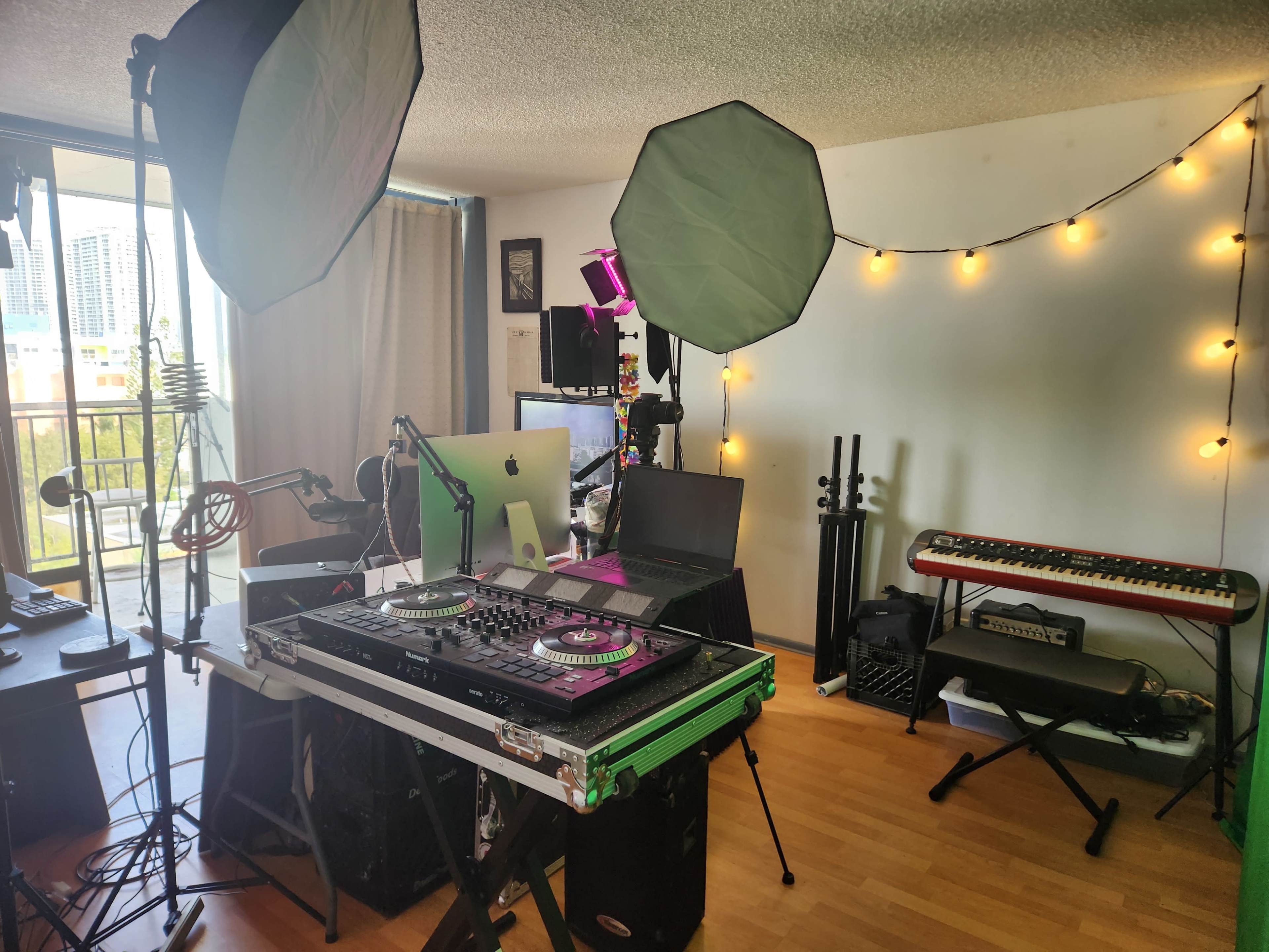 The image shows a home recording studio with a DJ setup, computer, lighting equipment, and musical instruments arranged in a well-lit room.