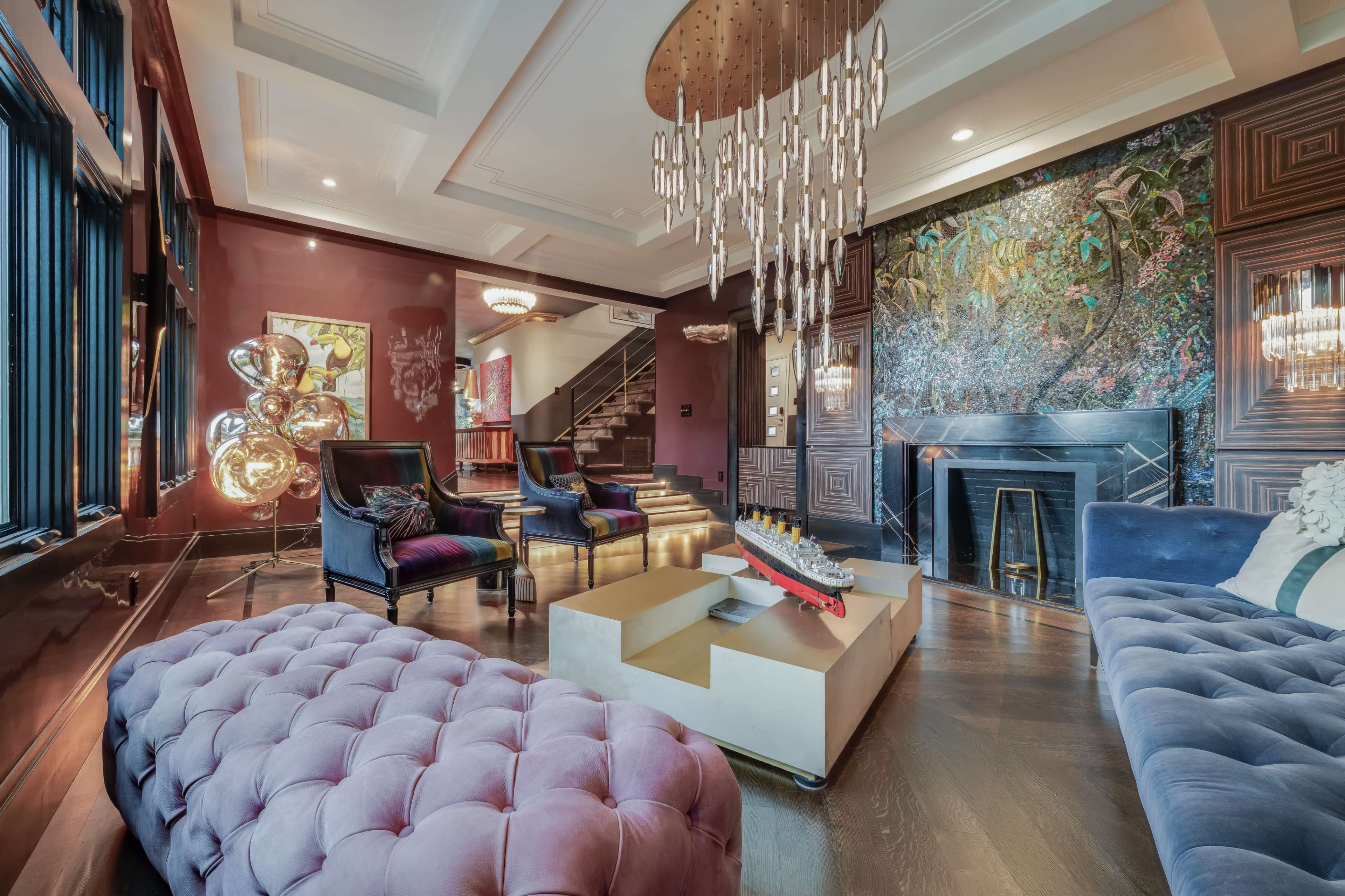 The image showcases a luxurious living room featuring velvet sofas, a large chandelier, and a decorative wall with a nature mural.