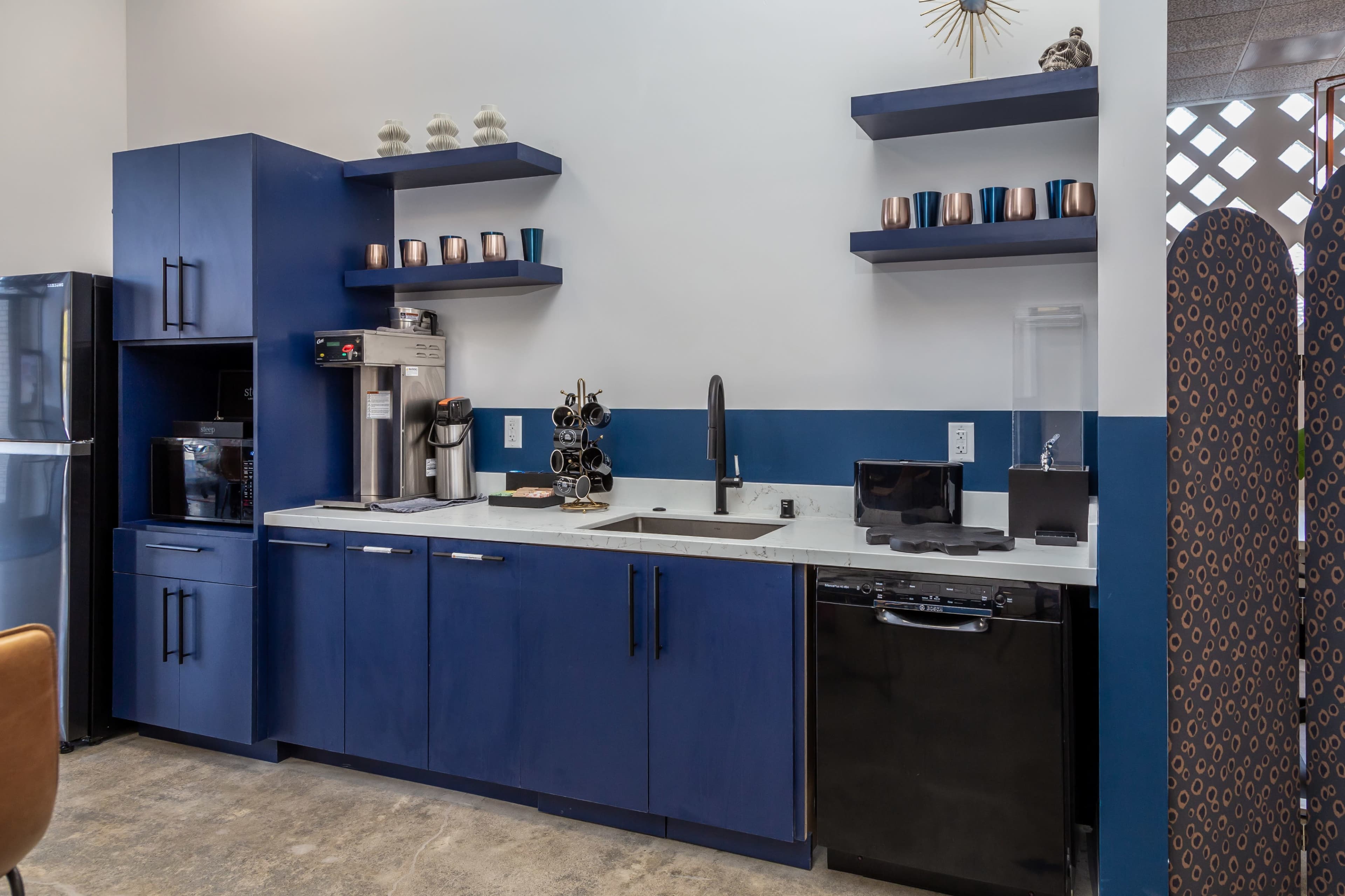 A modern kitchen area featuring blue cabinetry, a stainless steel sink, a coffee machine, and a microwave on the counter.
