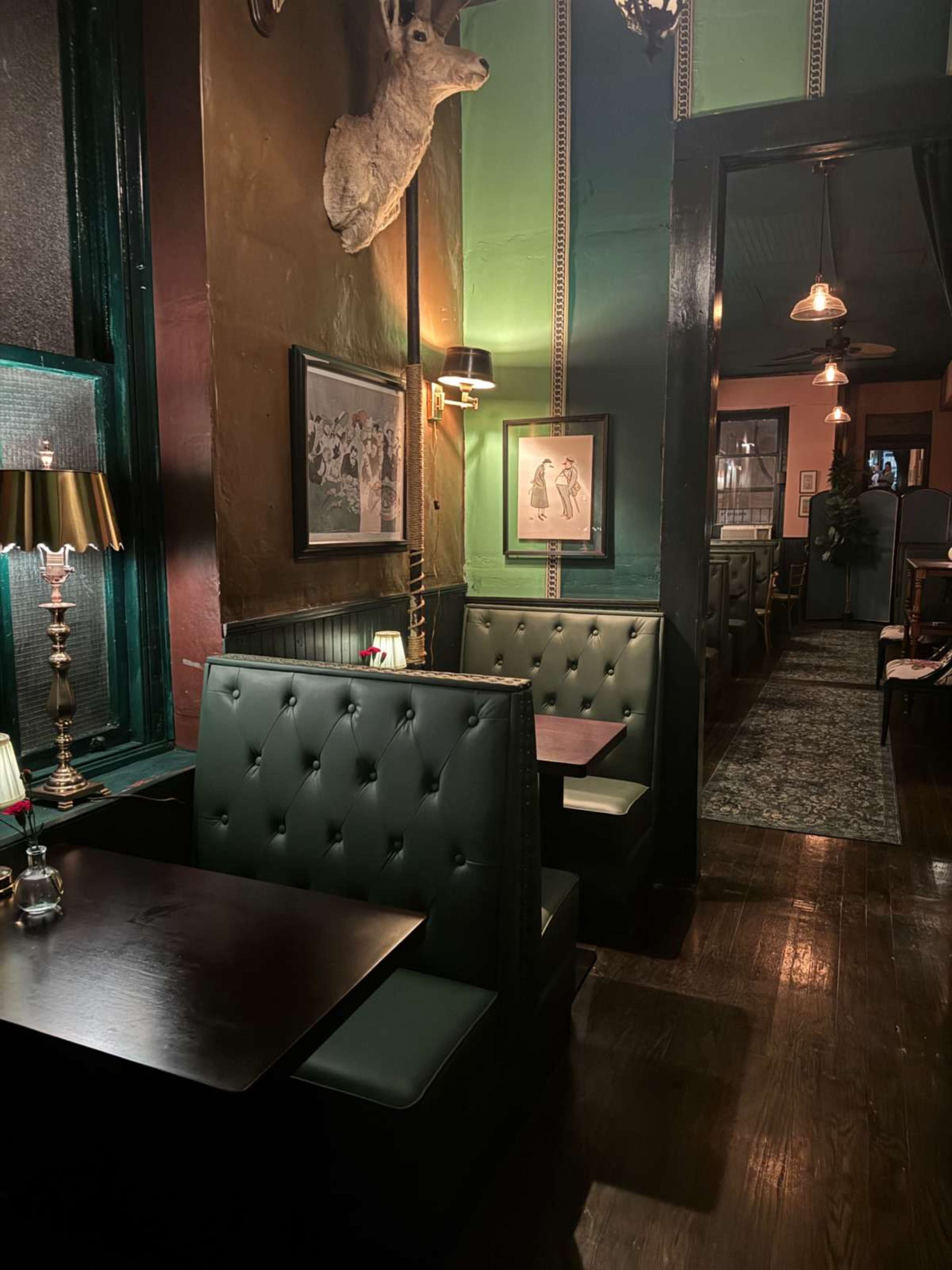 The image shows a dimly lit restaurant with green walls, leather booths, and framed photographs, leading towards a more brightly lit dining area.