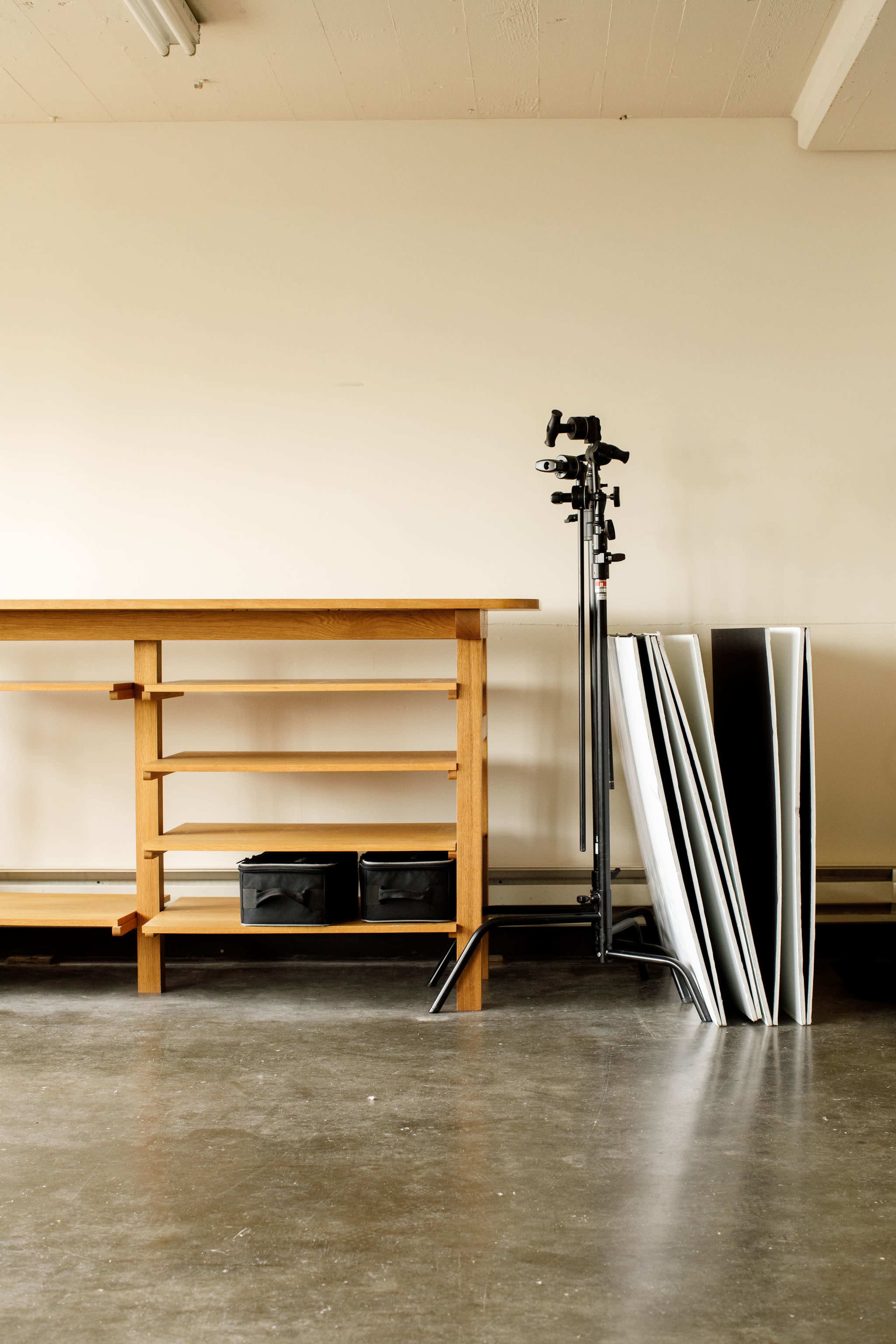A wooden workbench stands against a plain wall, accompanied by two black storage boxes and a set of large, leaning panels.