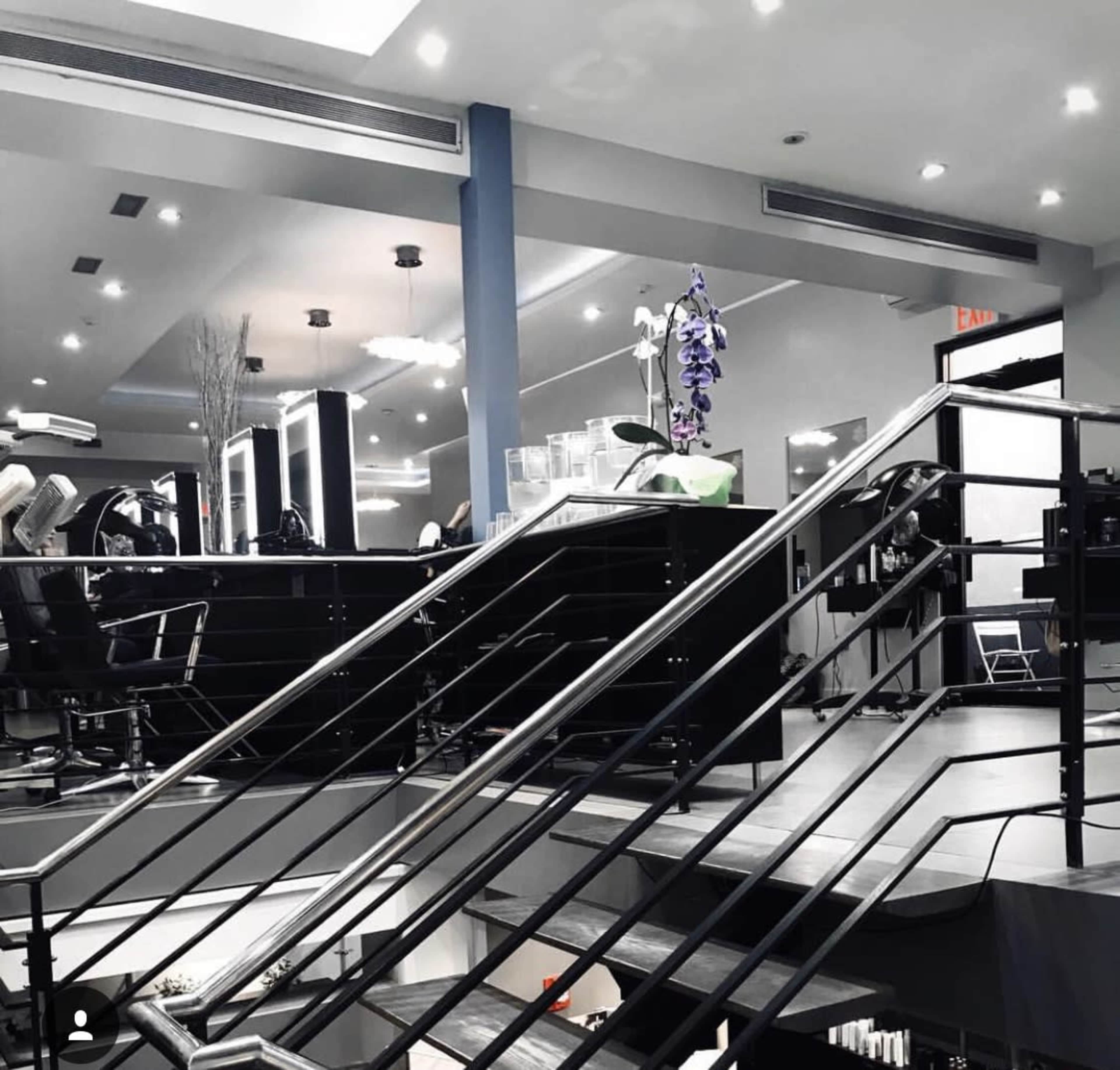 A modern salon interior with black styling chairs, a staircase, and decorative plants.