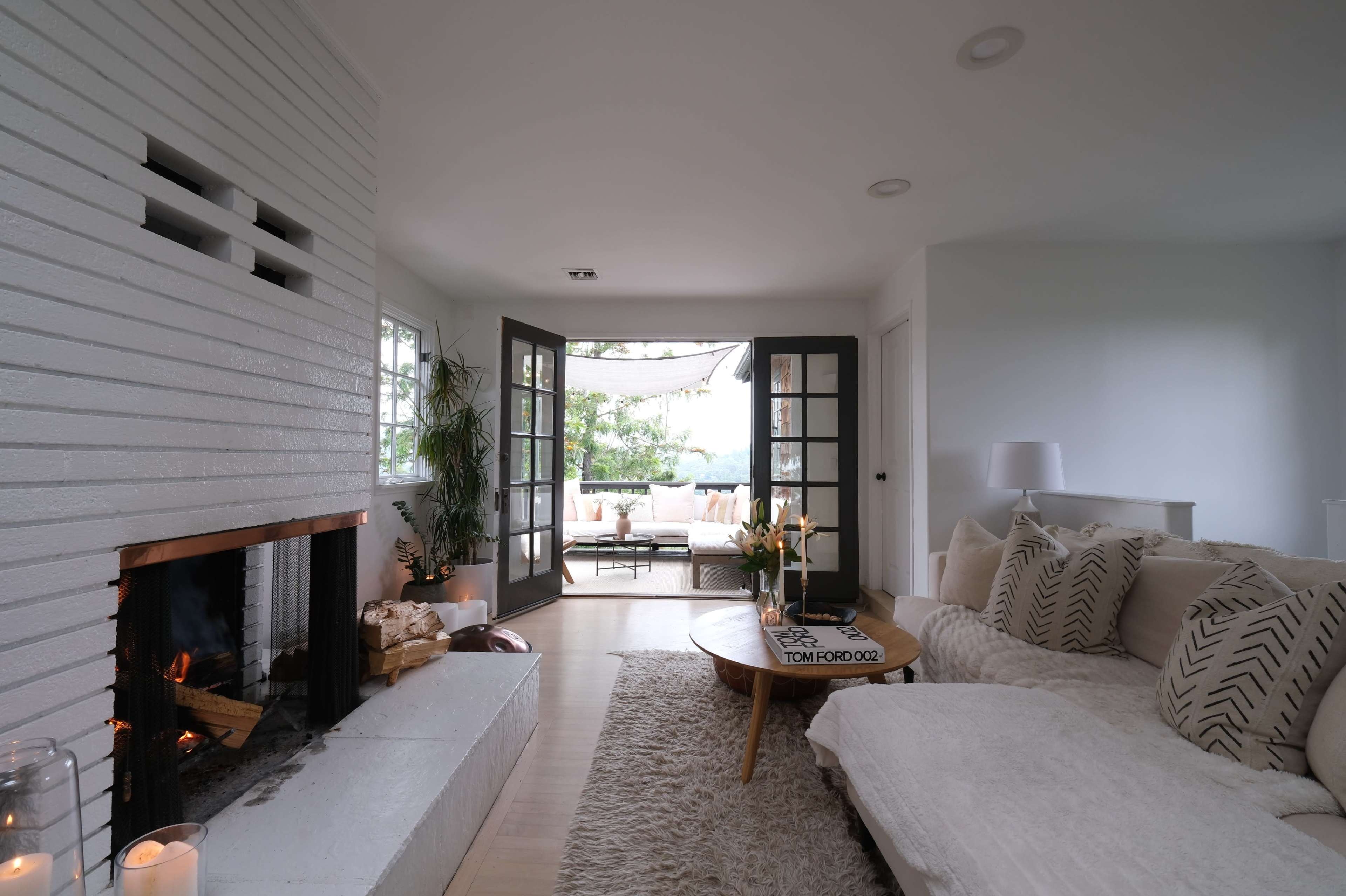 A modern living room with a white brick fireplace, a large sectional sofa, and a set of double doors leading to a patio area.