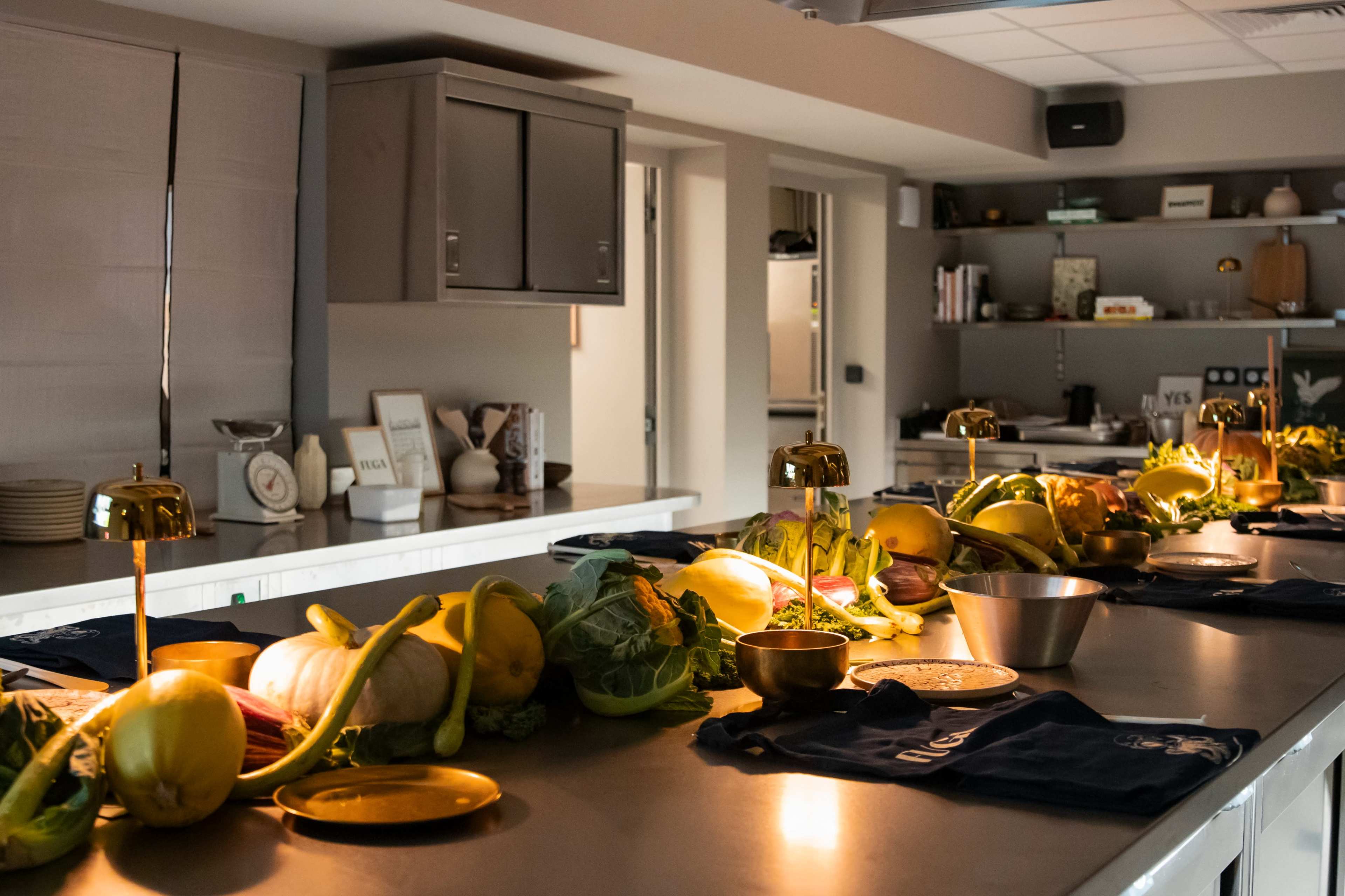A modern kitchen is arranged with an array of fresh vegetables and ingredients displayed on a long countertop under warm lighting.