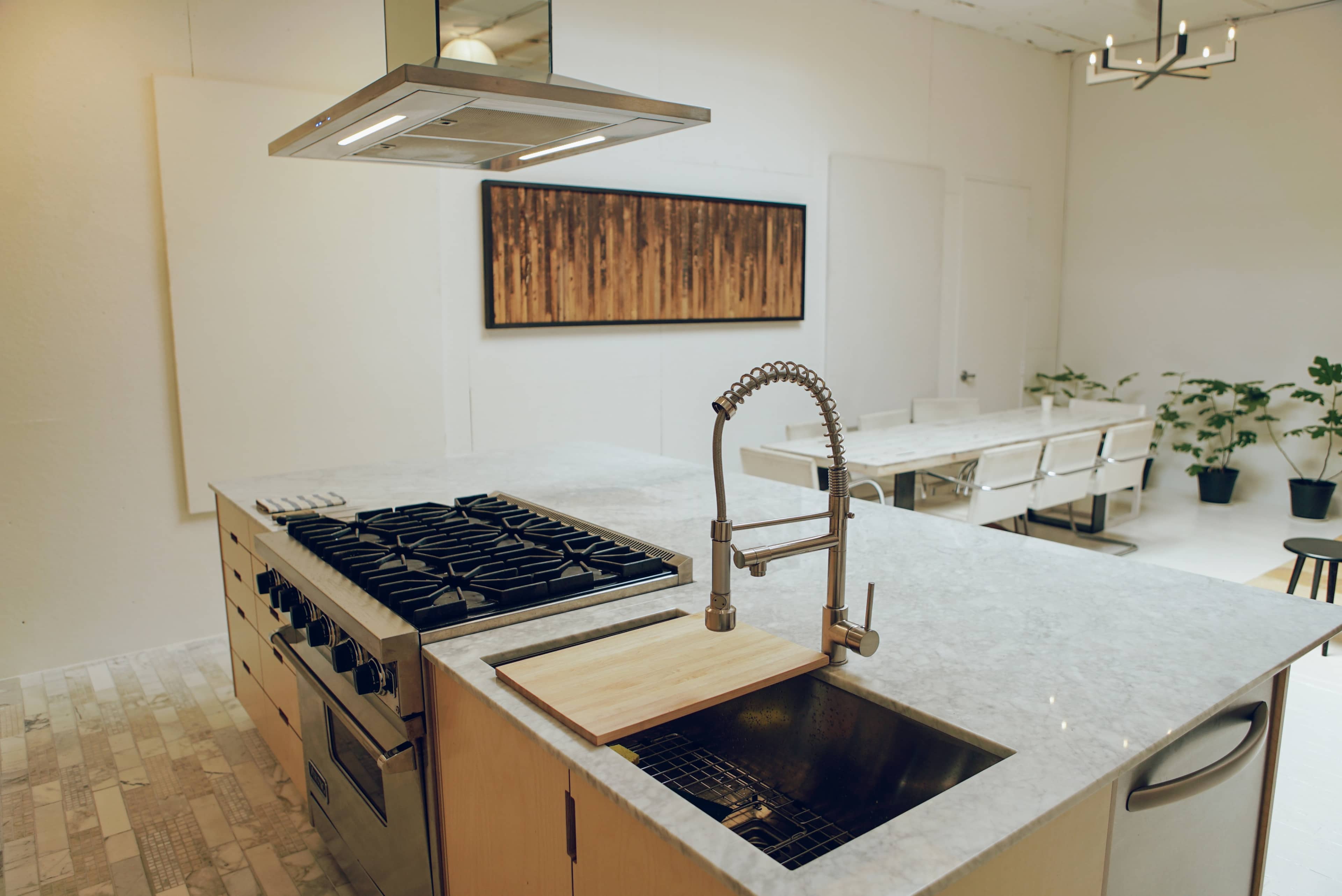 A modern kitchen with a central island featuring a gas cooktop and a sink, surrounded by minimalist decor and natural light.