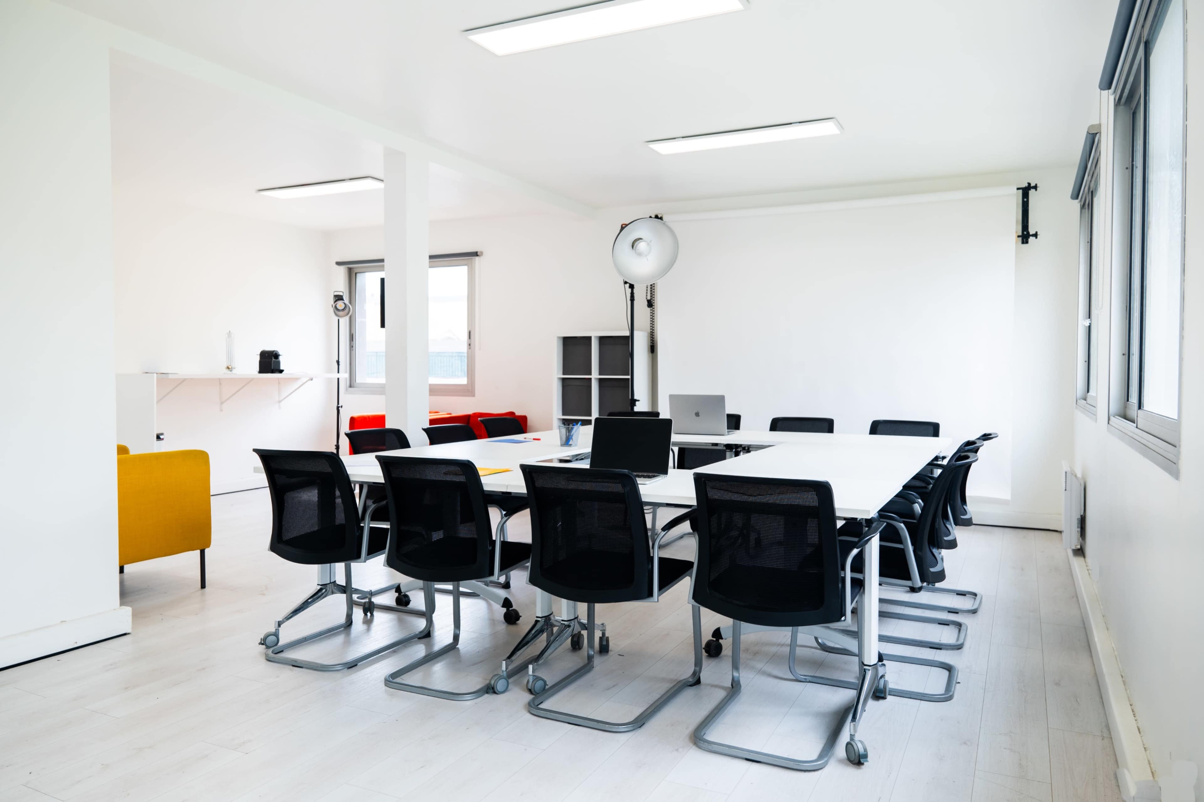 A modern conference room features a long table surrounded by black rolling chairs, with large windows and minimalistic decor.