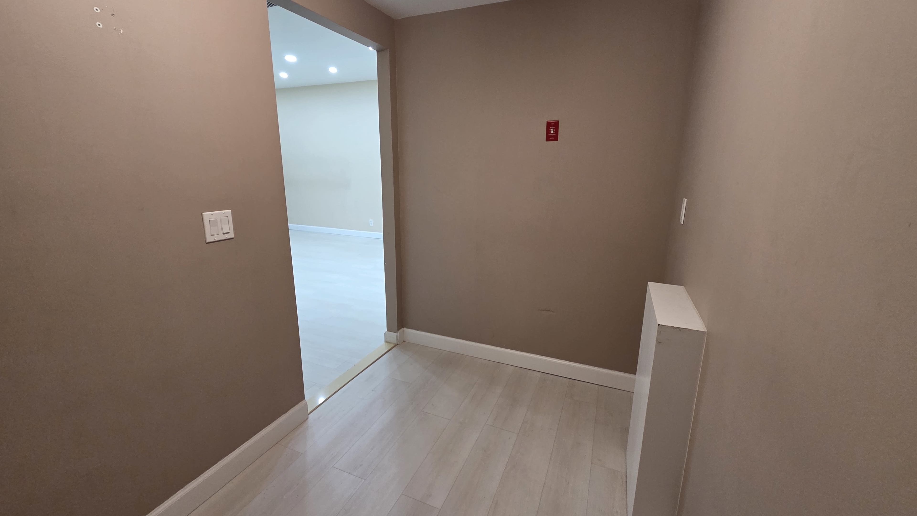 The image shows a narrow hallway leading to a room with light-colored walls and flooring.