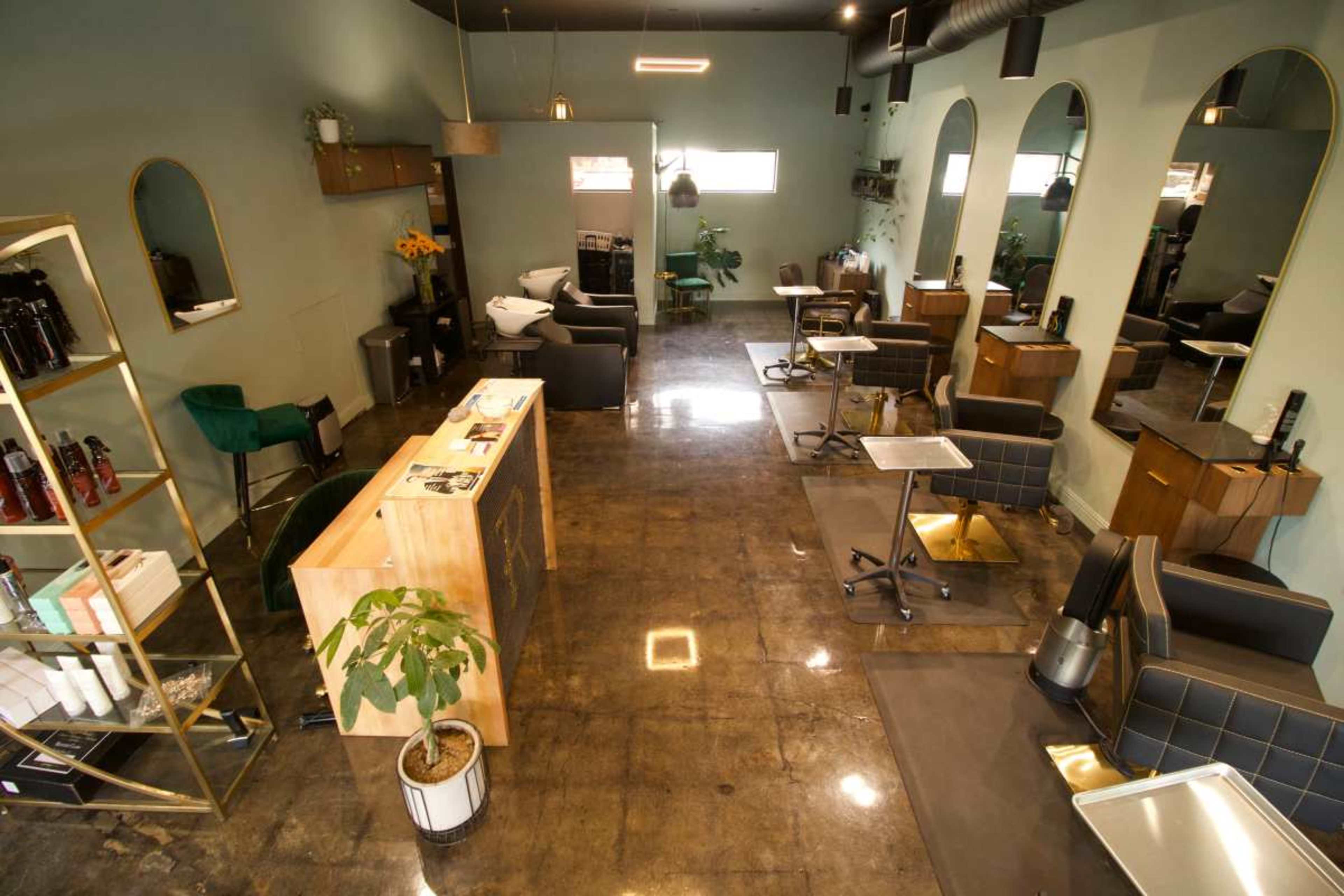 The image shows a modern salon interior featuring multiple styling stations, a reception area, and large windows that allow natural light to enter.