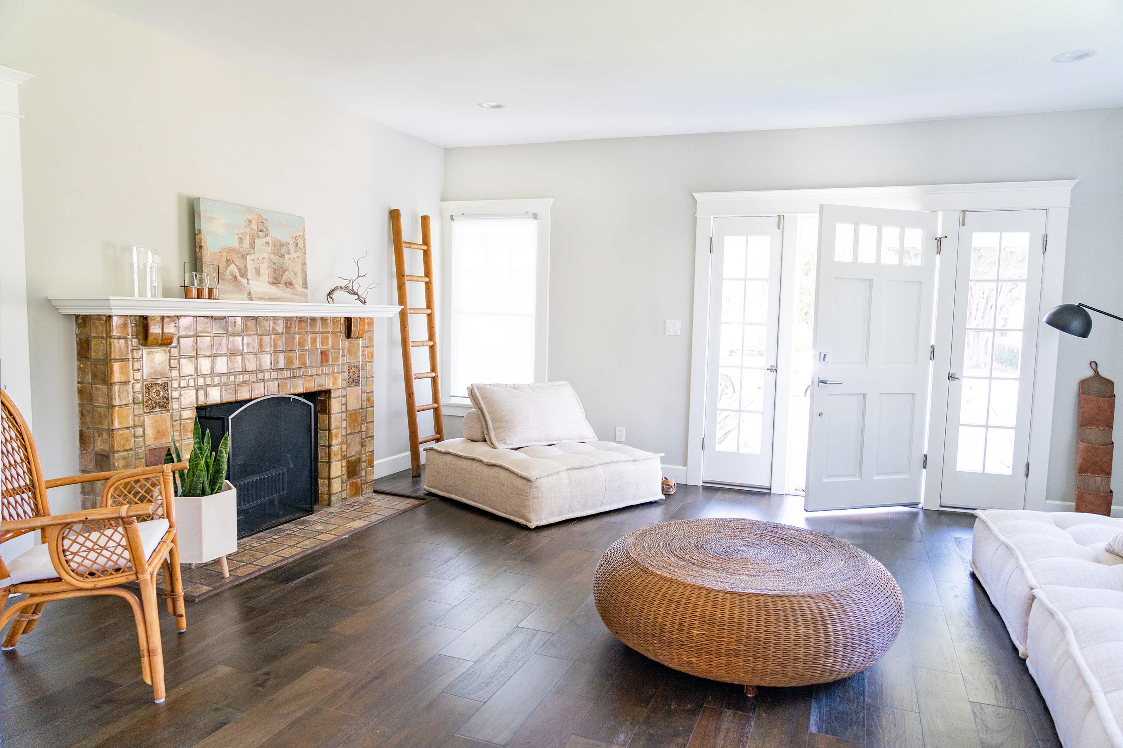 A bright living room featuring a brick fireplace, a woven ottoman, and large windows with double doors.