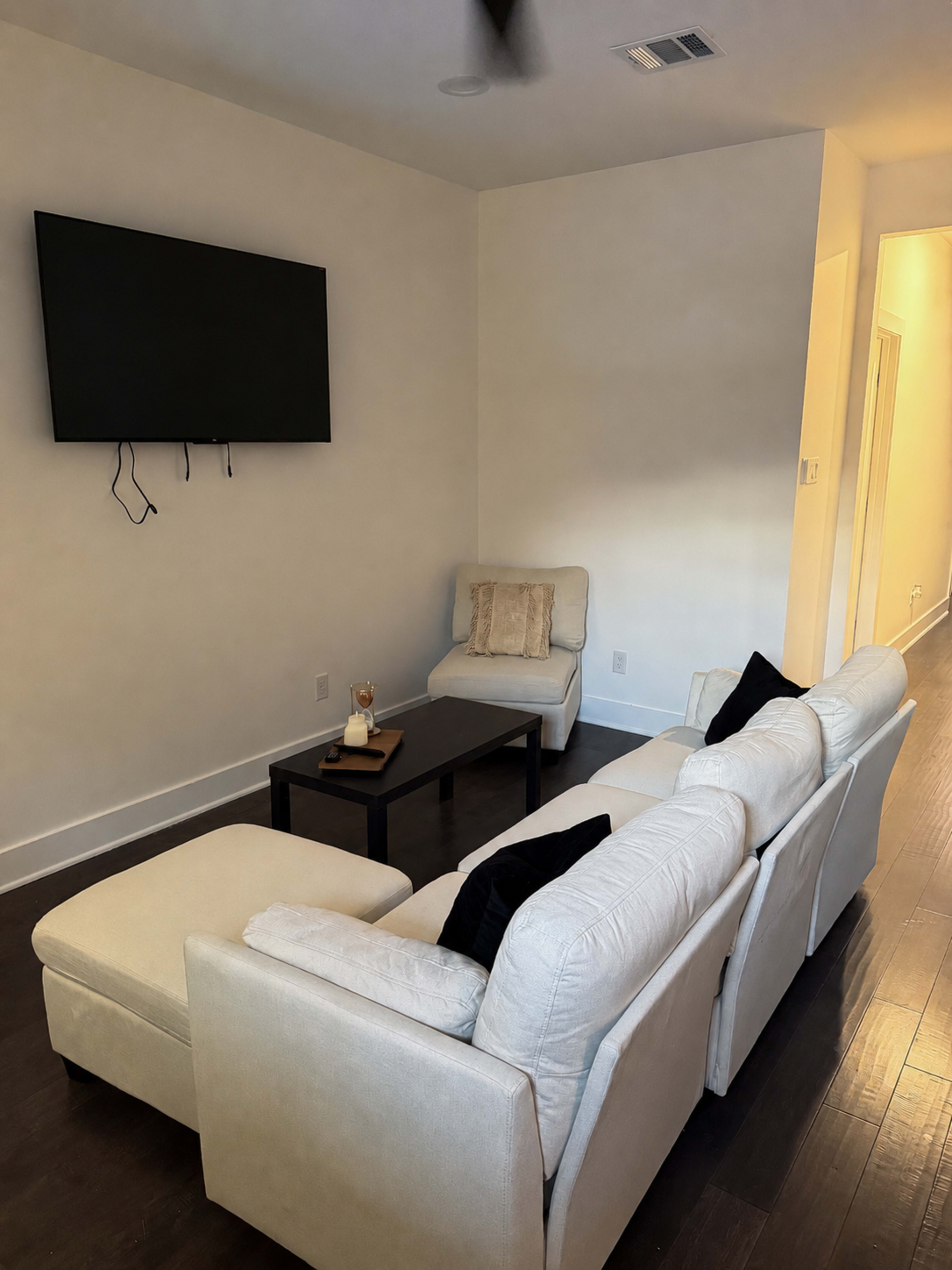 The image shows a minimalistic living room with a sectional sofa, a coffee table, and a wall-mounted television.