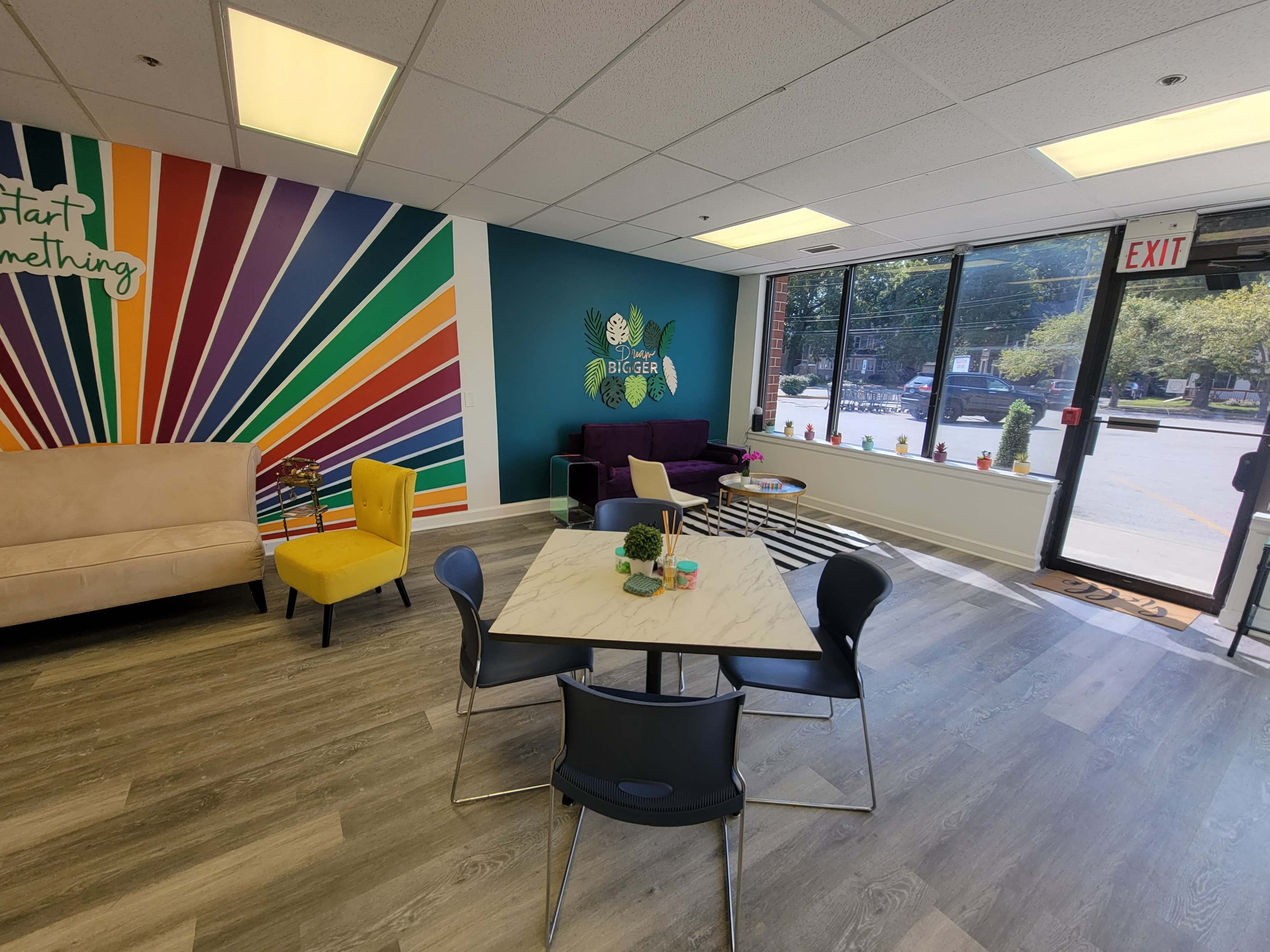 A colorful office space featuring a marble table with black chairs, a purple couch, and vibrant wall art in the background.