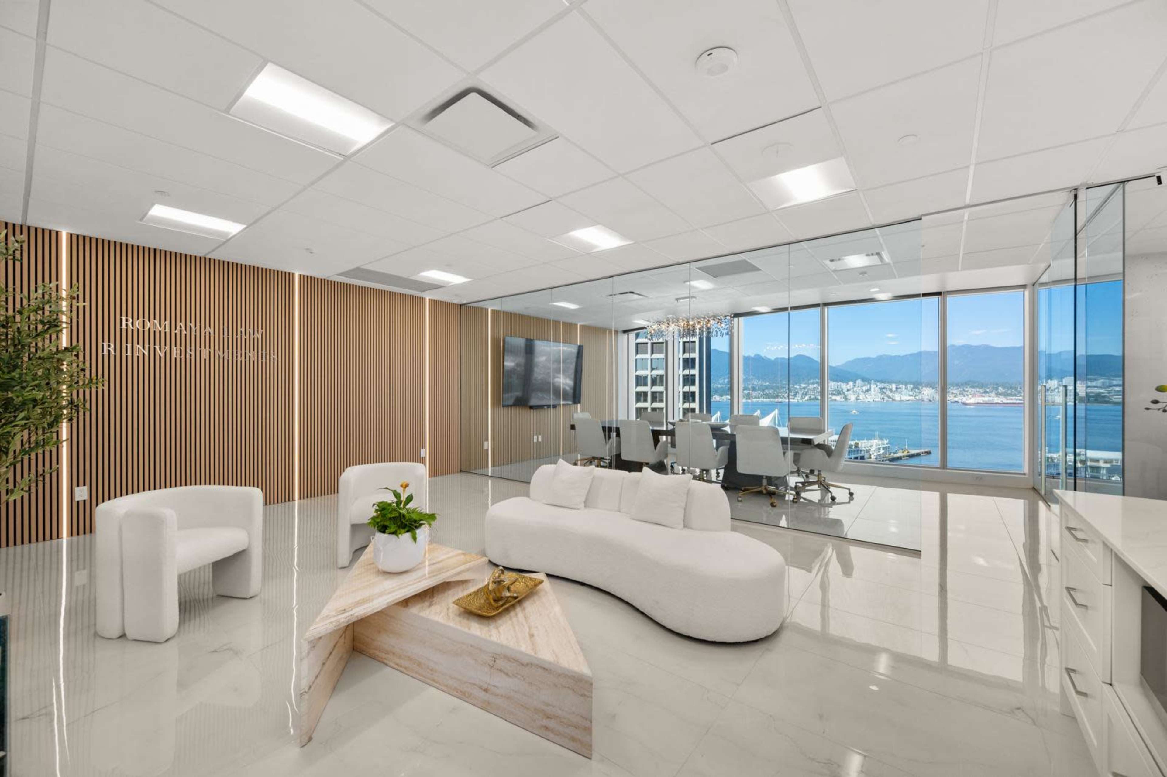 A modern office space features a spacious conference area with floor-to-ceiling windows overlooking a harbor and mountains.