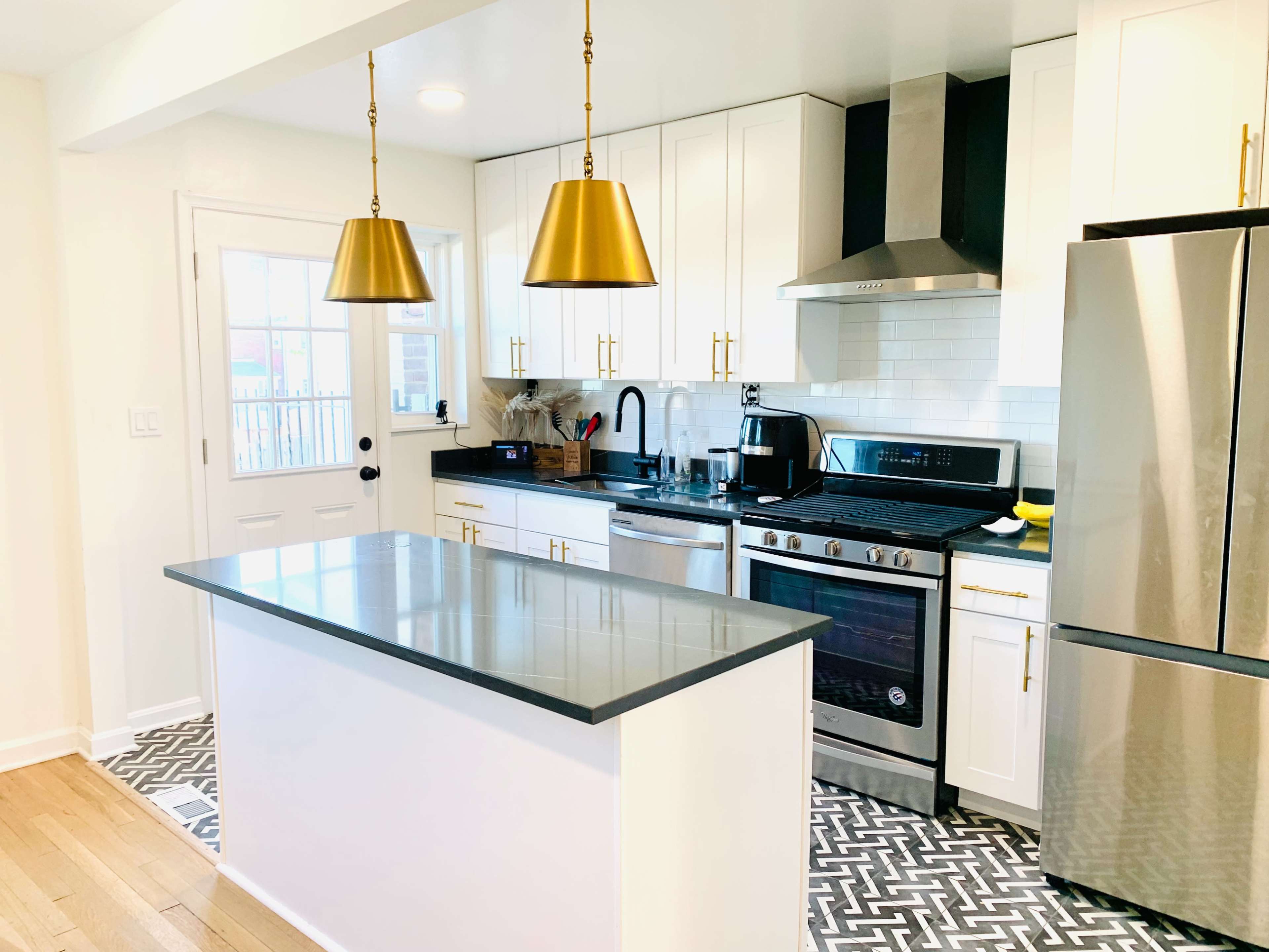 A modern kitchen with white cabinetry, a stainless steel stove, and a center island featuring gray countertops and two gold pendant lights above.