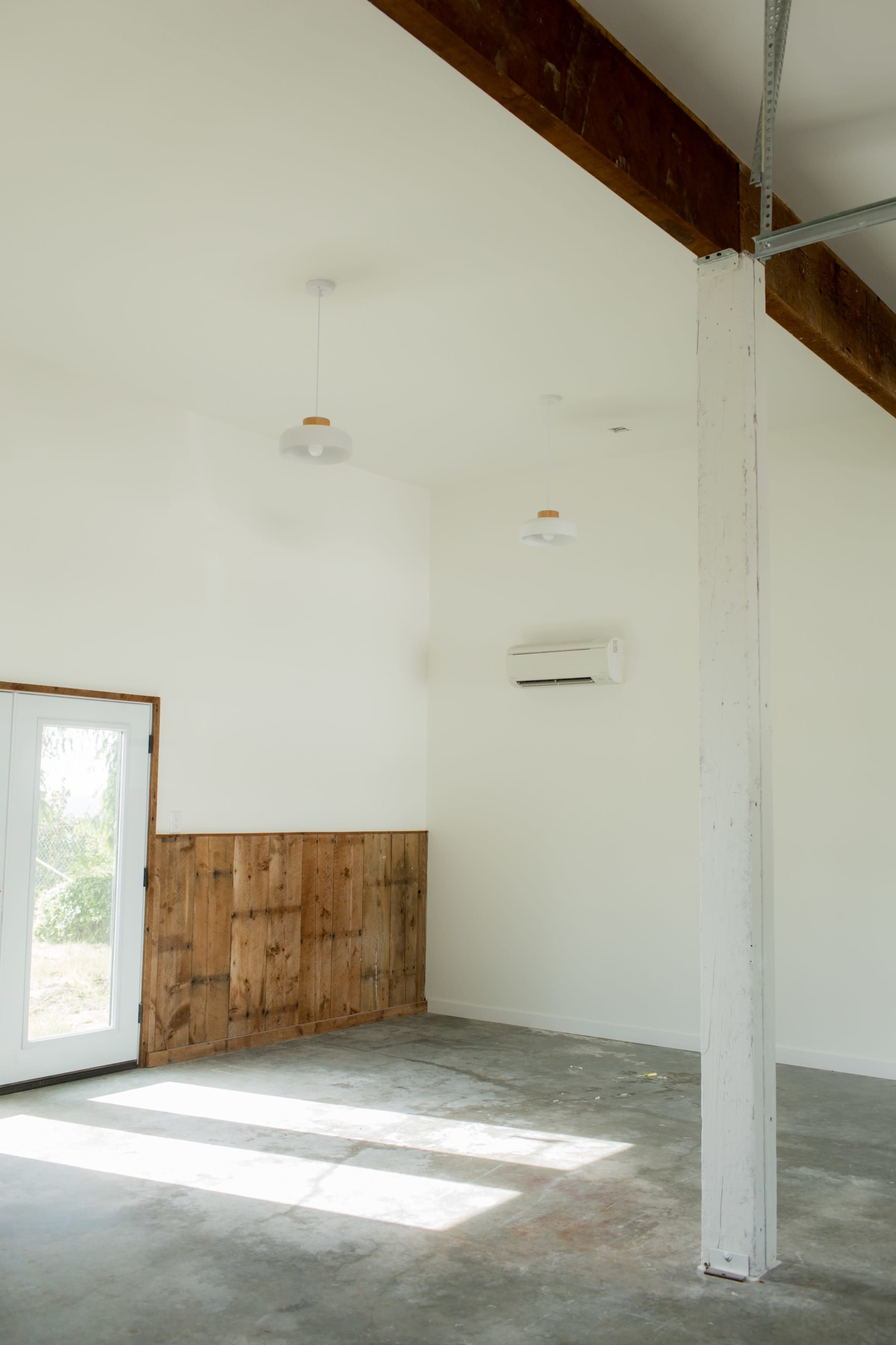 The image features an empty room with white walls, a wooden accent wall, a ceiling light fixture, and an air conditioning unit.