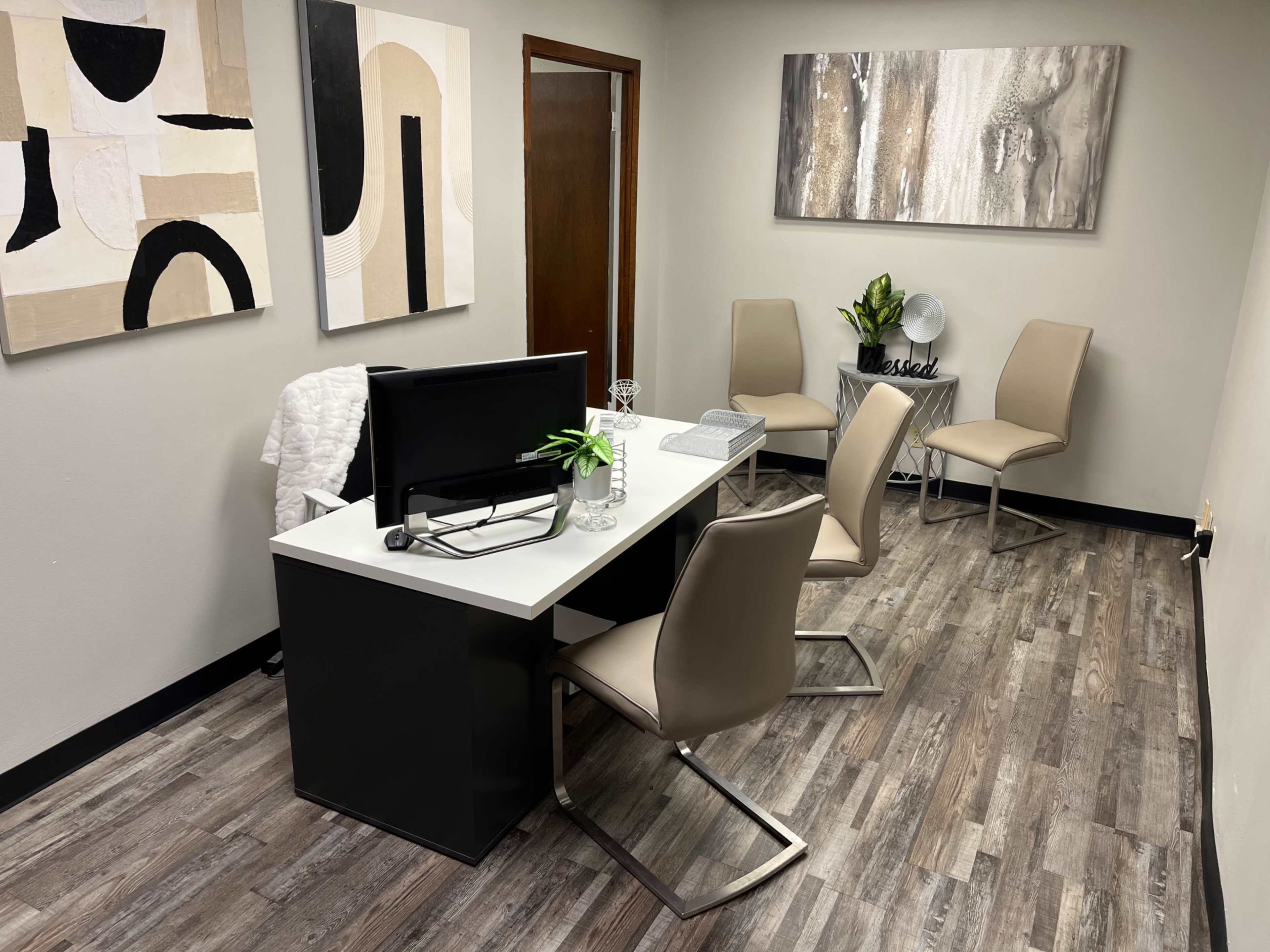 A modern office with a white desk, a computer, four chairs, and abstract wall art.